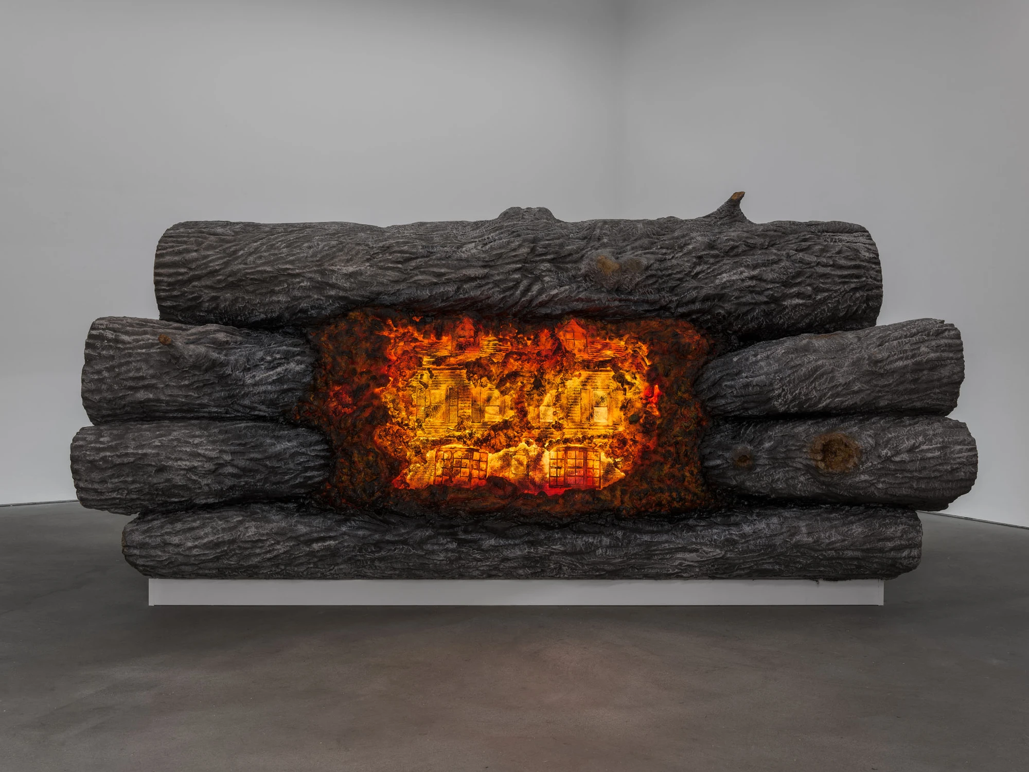 Cold Front by Trey Abdella at Kraupa-Tuskany Zeidler — A sculptural assemblage featuring stacked charred timber logs arranged horizontally, with a glowing aperture at center revealing a printed domestic interior...