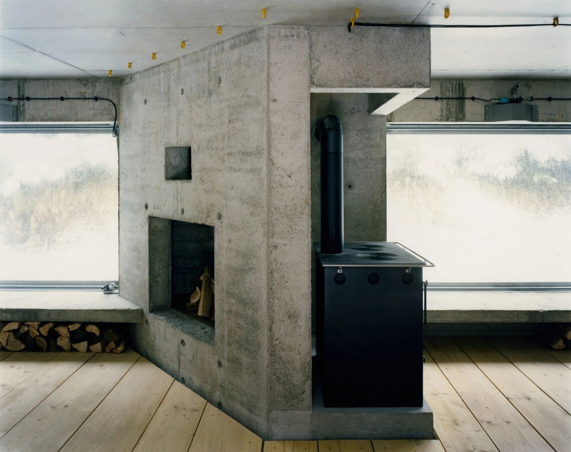 Hut on Fichtelberg by AFF Architekten — Interior view of the Hutznhaisl revealing the spatial organization around a black steel stove.
