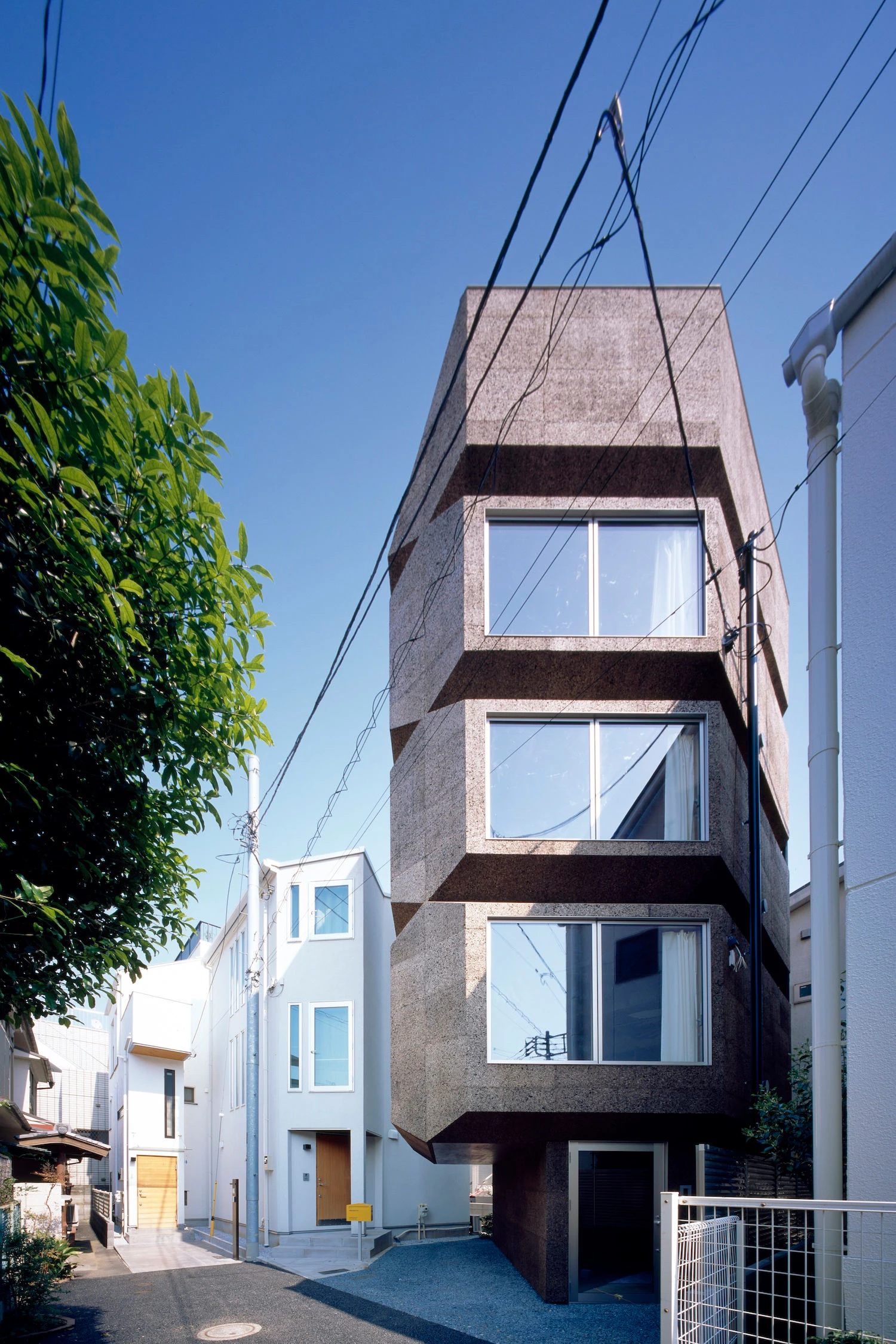 Bay Window Tower House by Takaaki Fuji + Yuko Fuji Architecture — The Bay Window Tower House presents its full octagonal profile against a clear sky, the stacked bay window ledges creating pronounced horizontal shadow...