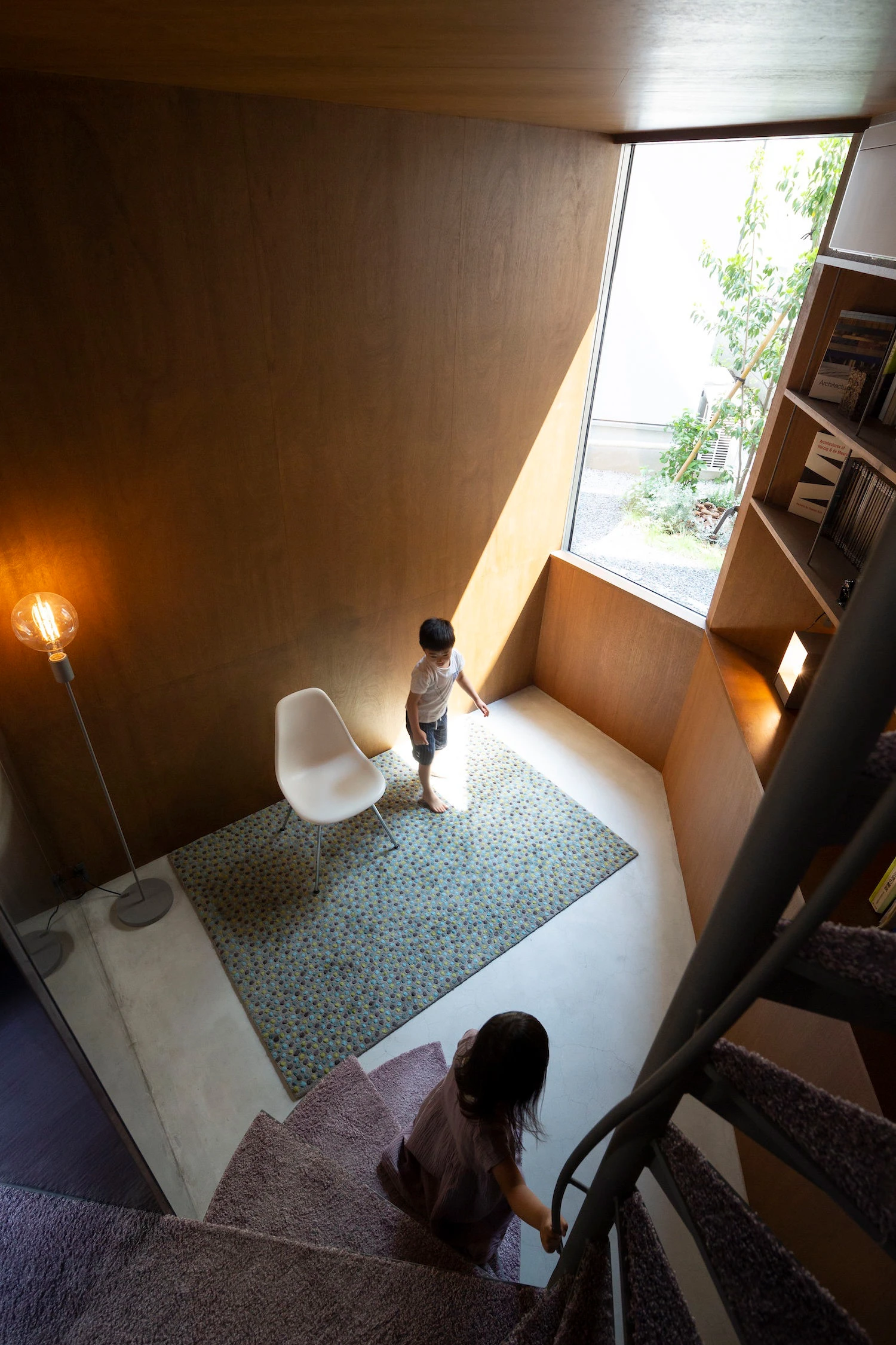 Bay Window Tower House by Takaaki Fuji + Yuko Fuji Architecture — Overhead view of the Bay Window Tower House's interior passage, showing a child descending stairs while another explores the ground-floor bay window ledge.