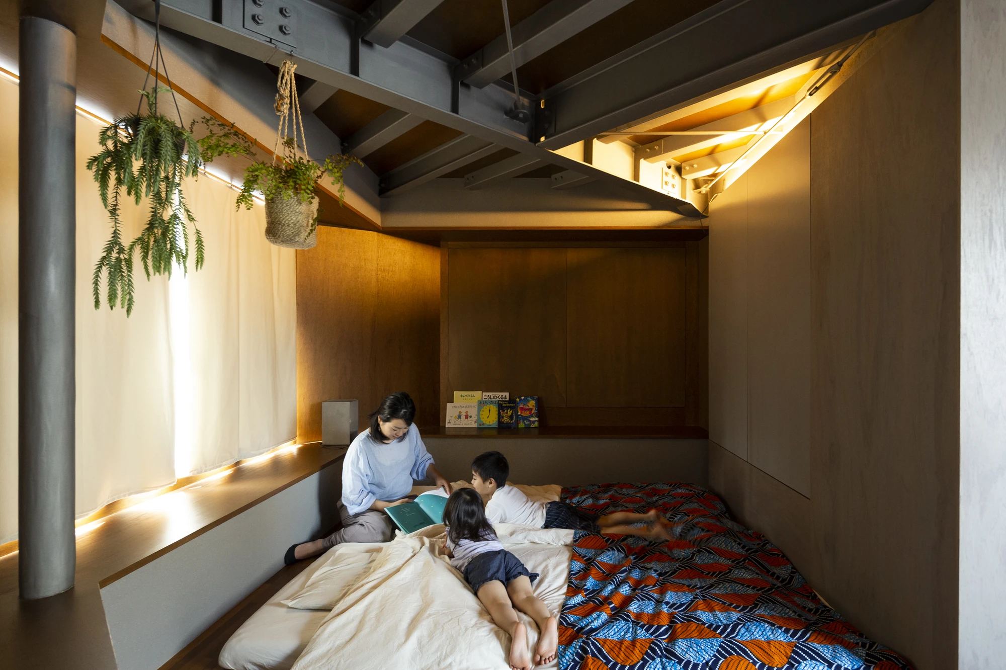 Bay Window Tower House by Takaaki Fuji + Yuko Fuji Architecture — A mother and two children occupy a bay window alcove on an upper floor, reading and resting on layered bedding.