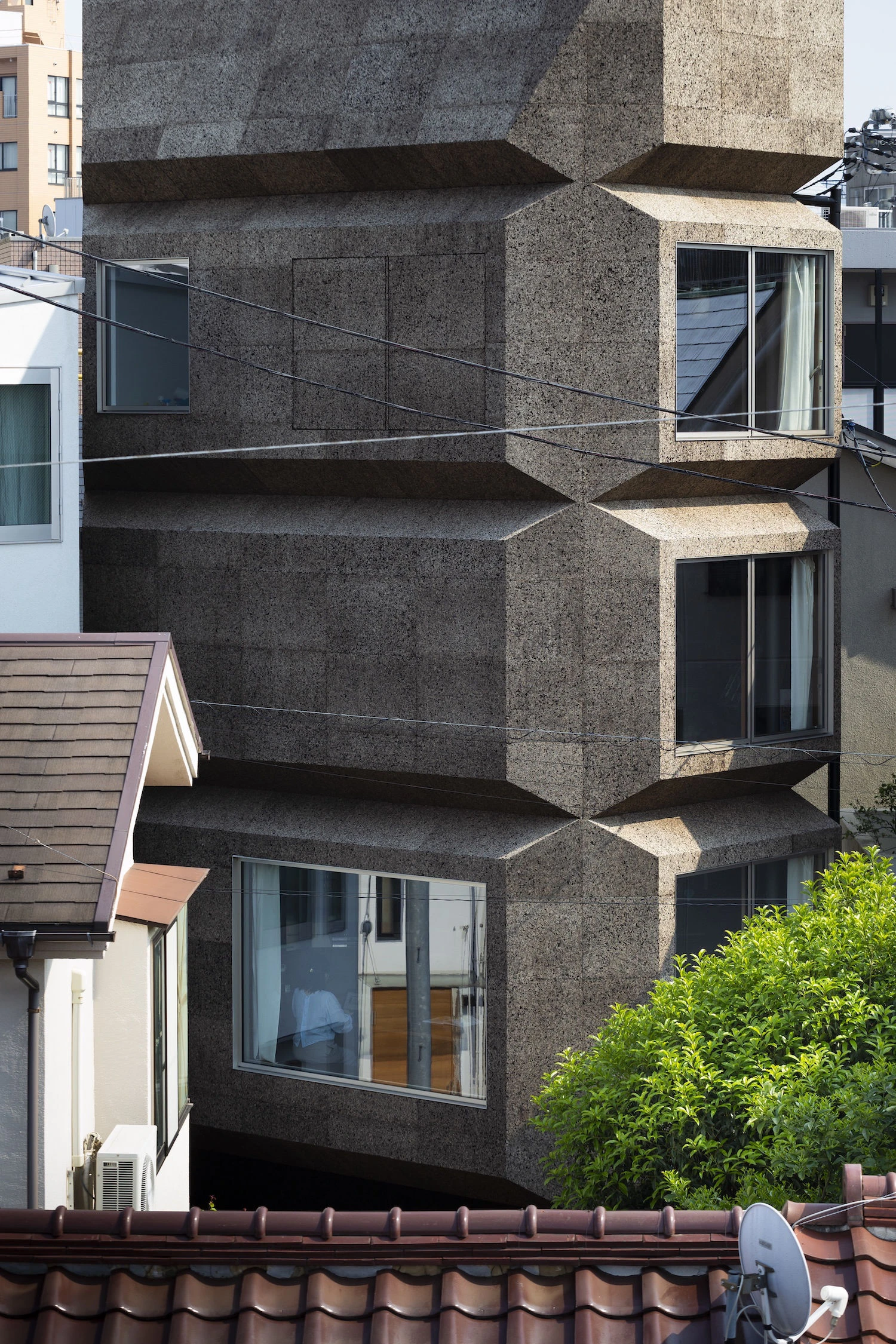 Bay Window Tower House by Takaaki Fuji + Yuko Fuji Architecture — The Bay Window Tower House presents a monolithic facade of dark textured aggregate concrete, its surface articulated by eight chamfered corners creating an...