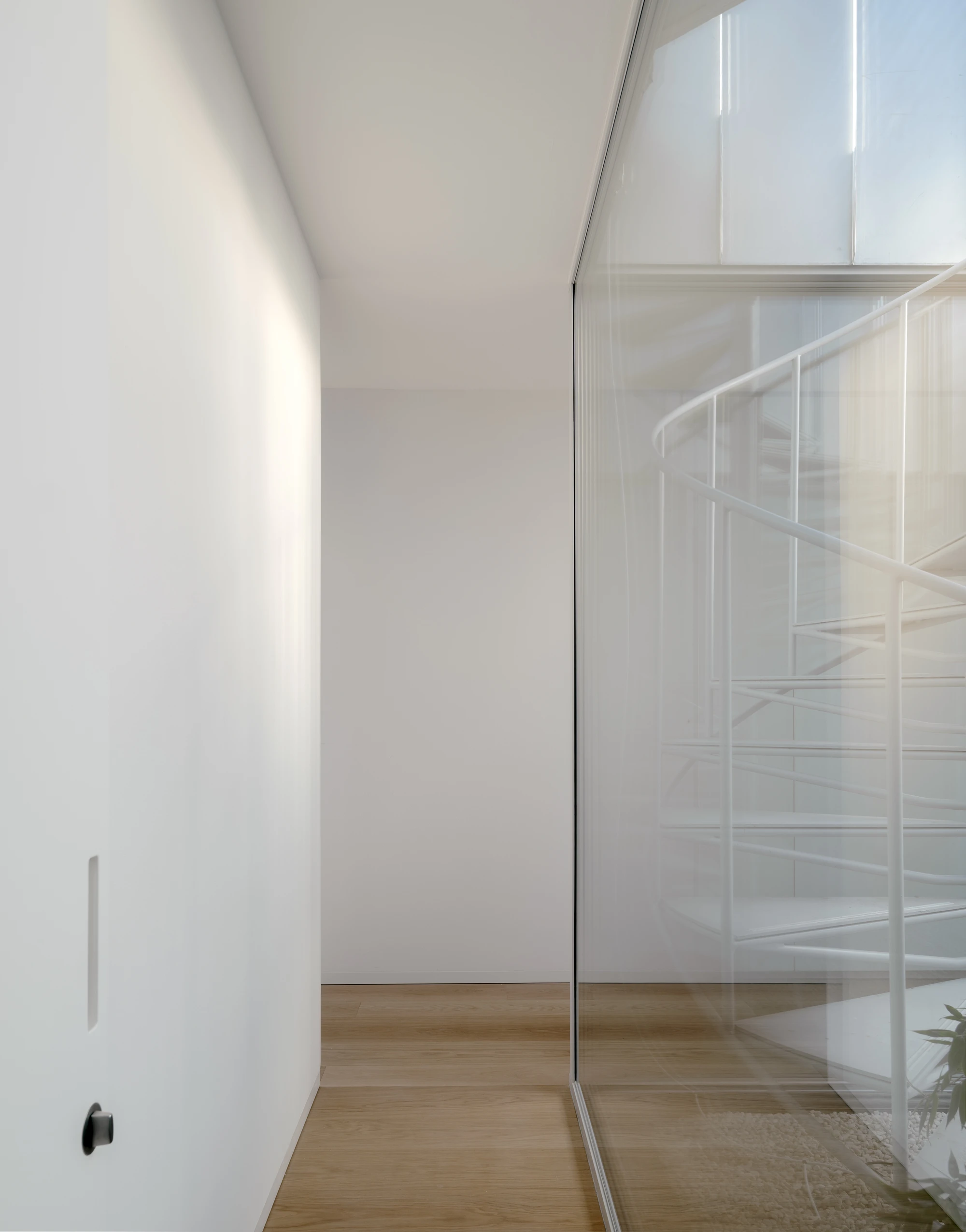 Ursulastraße 6 by Studio Mark Randel — A narrow passage framed by a white plaster wall on the left and a frameless glass sliding door with minimal aluminum mullions on the right.
