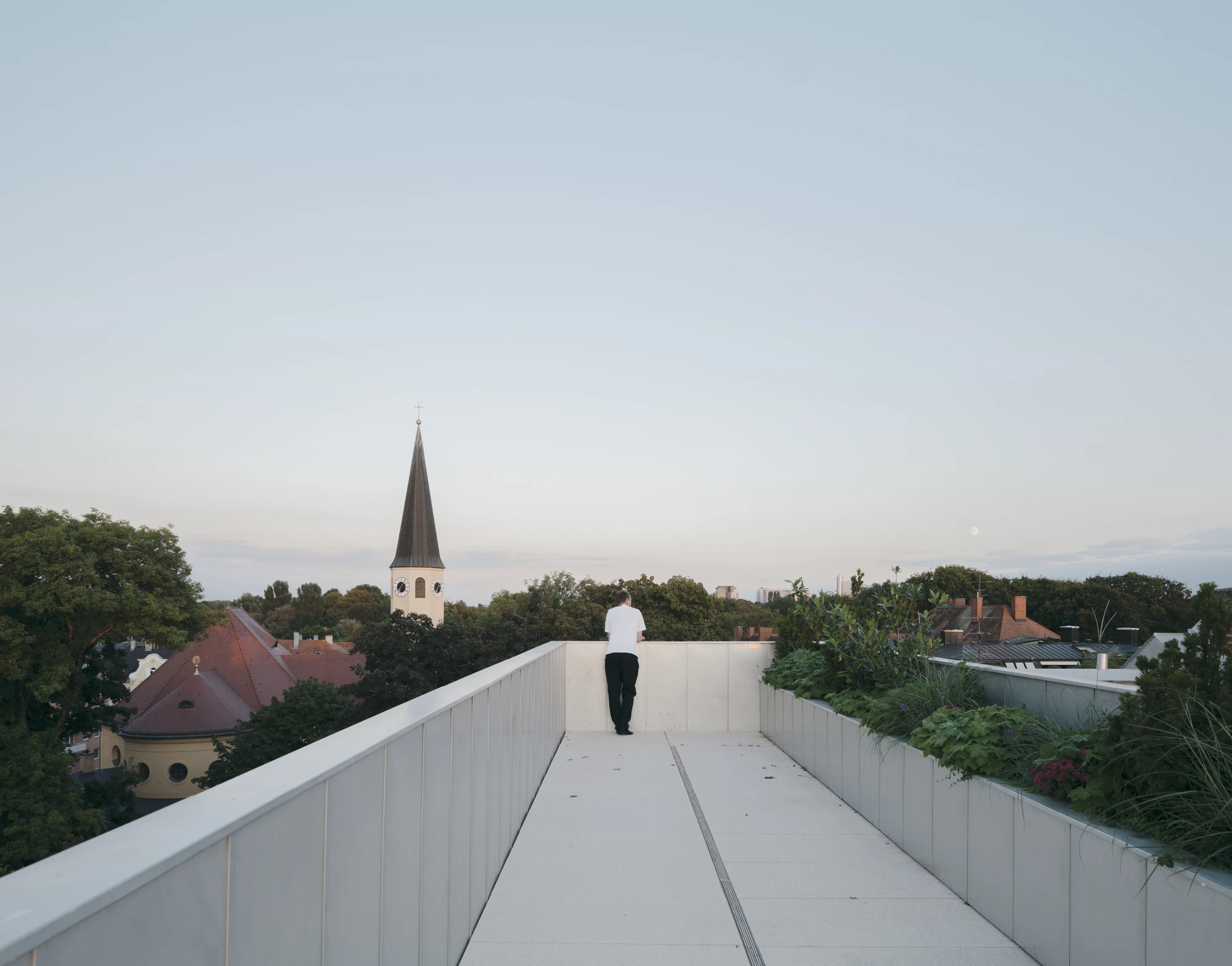 Ursulastraße 6 by Studio Mark Randel — A figure jogs across a white polycarbonate bridge spanning the roofscape of Ursulastraße 6, connecting interior spaces while framing views toward the...