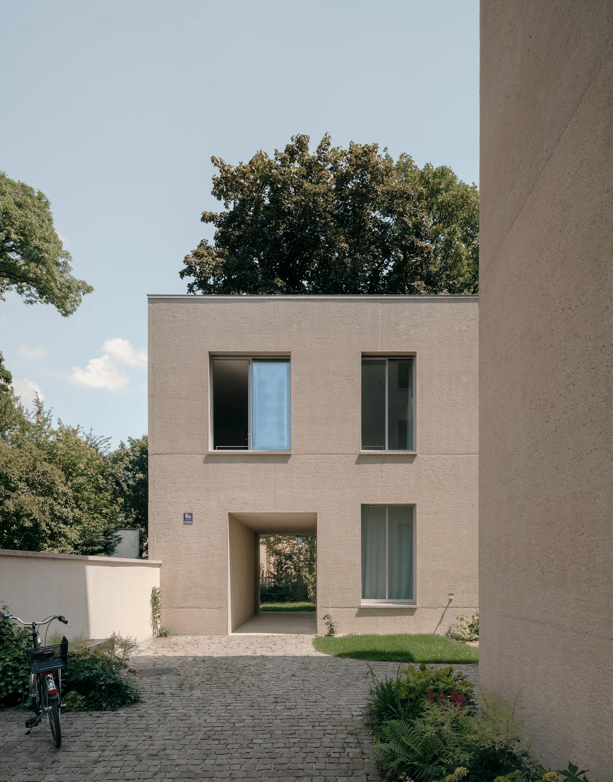 Ursulastraße 6 by Studio Mark Randel — The front facade of Ursulastraße 6 presents a rendered brick exterior in warm taupe, punctuated by two horizontal bands of fenestration.