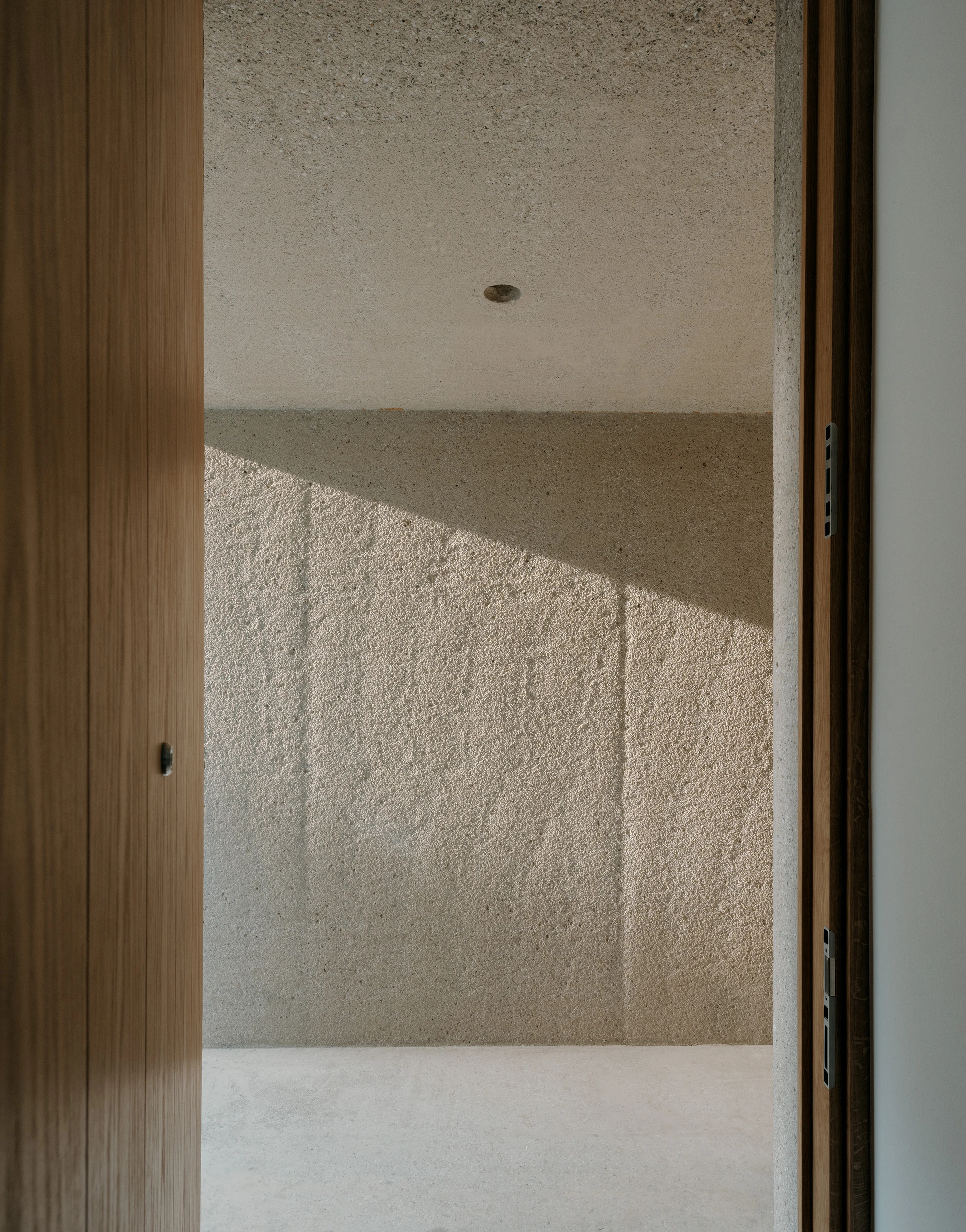 Ursulastraße 6 by Studio Mark Randel — A threshold framed by timber doorjambs reveals interior surfaces organized by material and light.