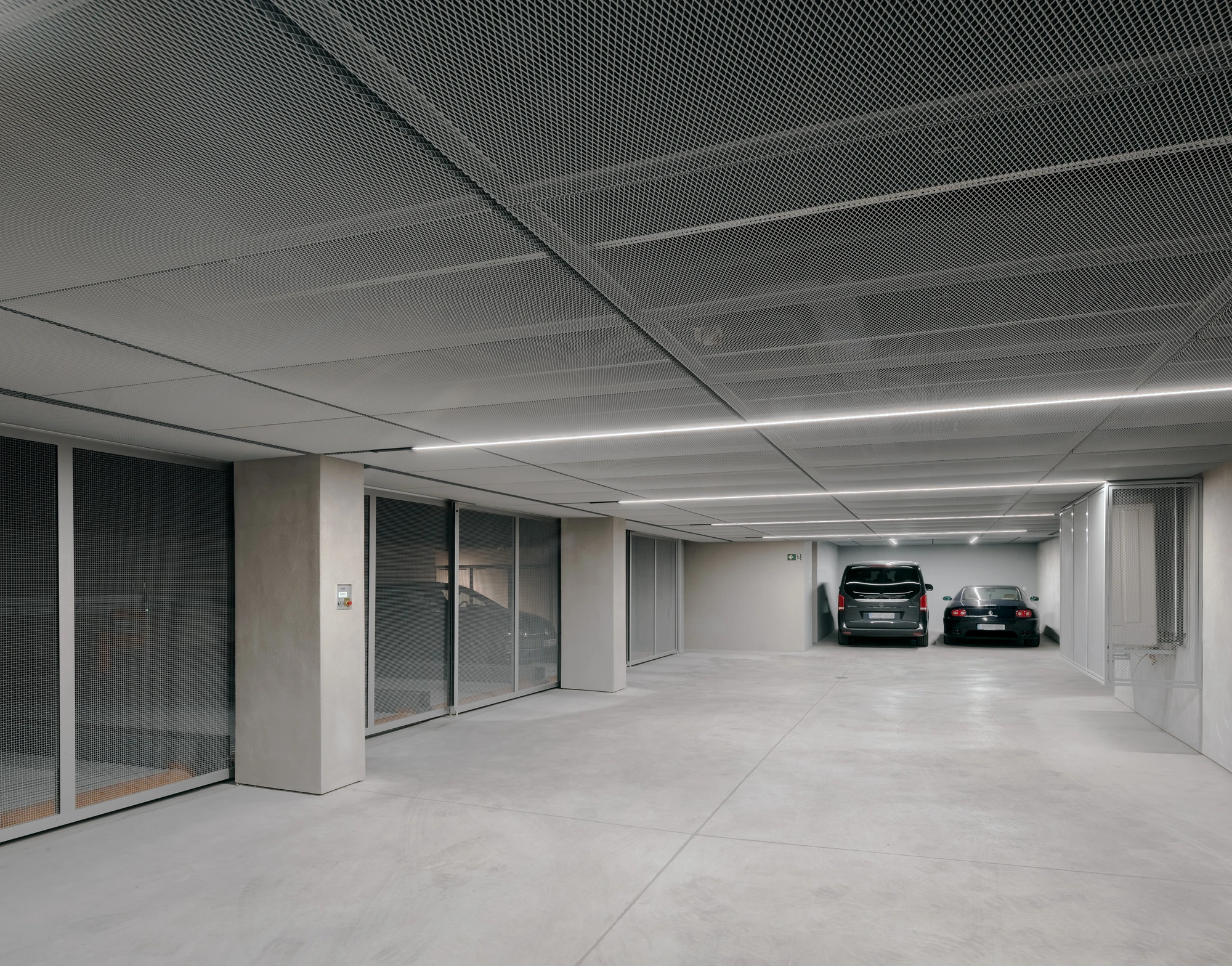 Ursulastraße 6 by Studio Mark Randel — A subterranean parking garage with linear fluorescent ceiling fixtures casting even illumination across a polished concrete floor.