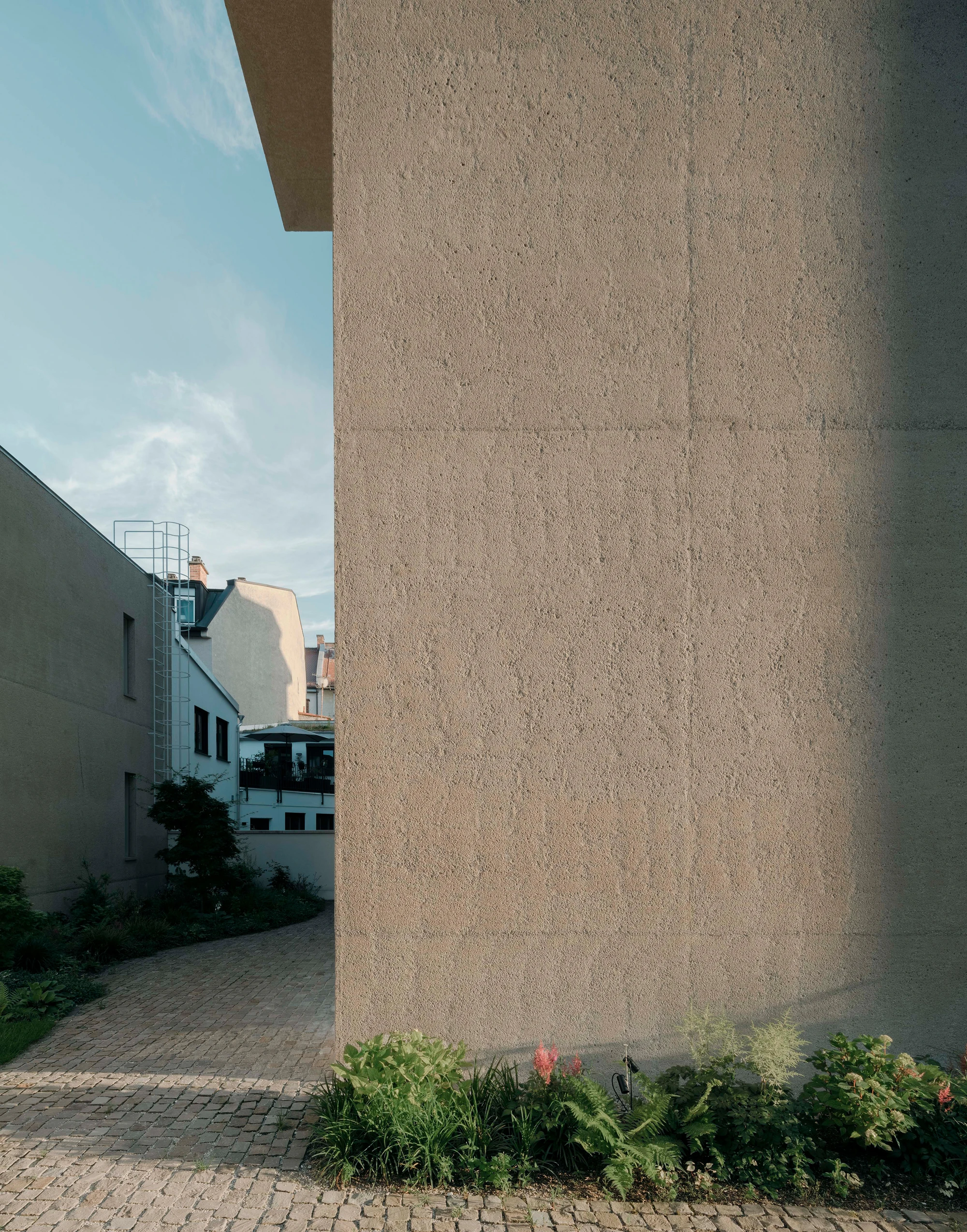 Ursulastraße 6 by Studio Mark Randel — A monolithic render facade dominates the composition, its textured surface catching afternoon light across the full height of the frame.