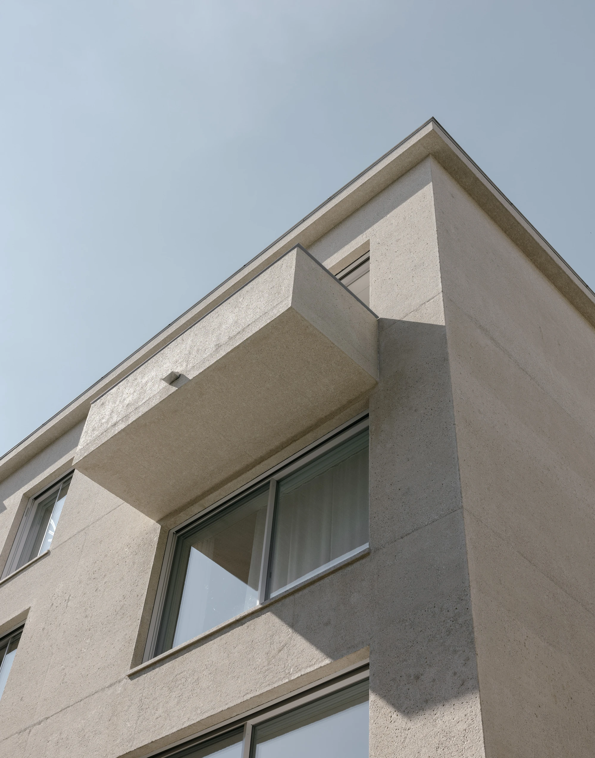 Ursulastraße 6 by Studio Mark Randel — The corner elevation reveals the building's monolithic concrete structure, with a cantilevered balcony casting a sharp shadow across the light render facade.