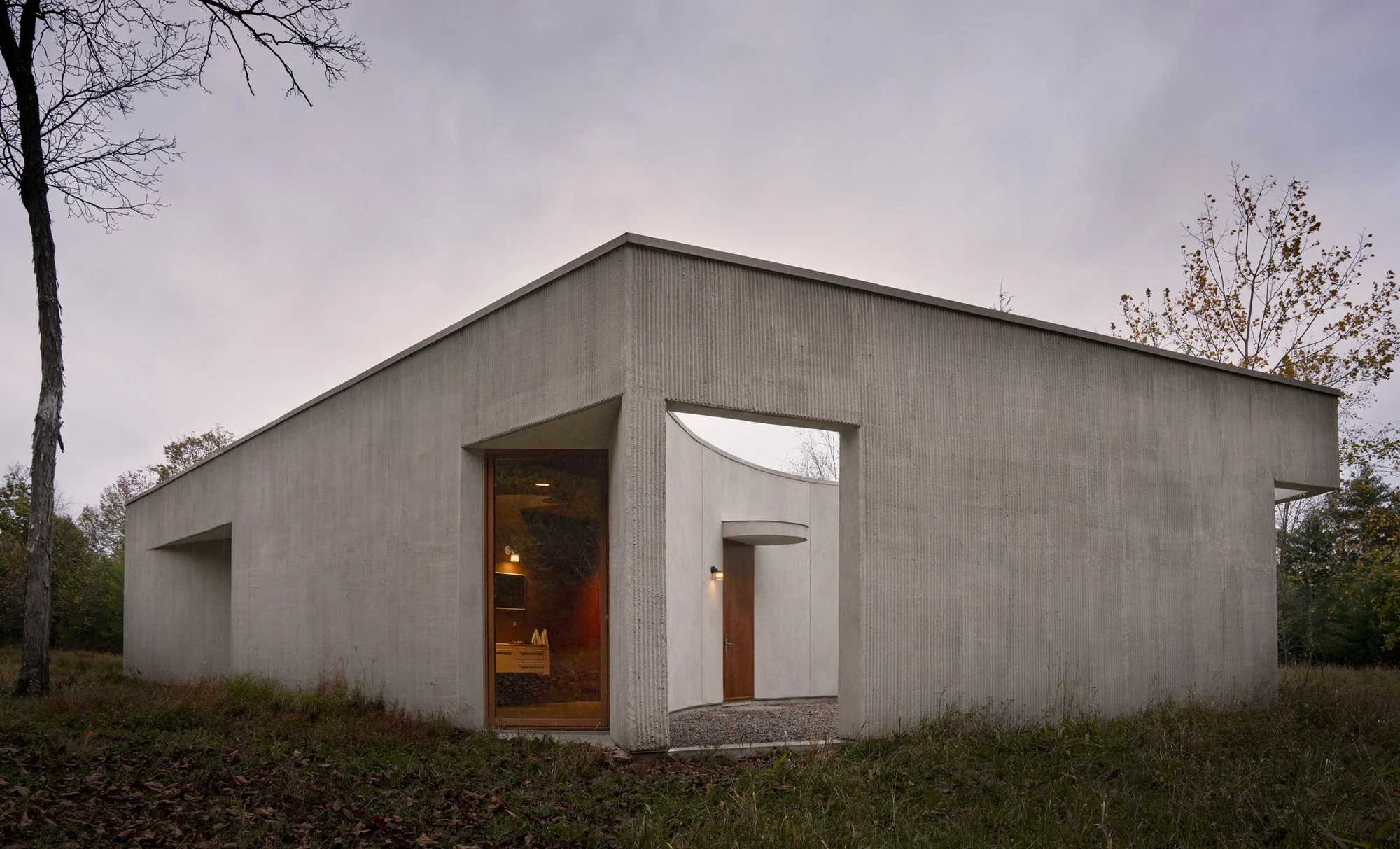 Vipp Upstate by Johnston Marklee — The rendered concrete structure presents a geometric volumetric form defined by two curved walls that create a partial enclosure.