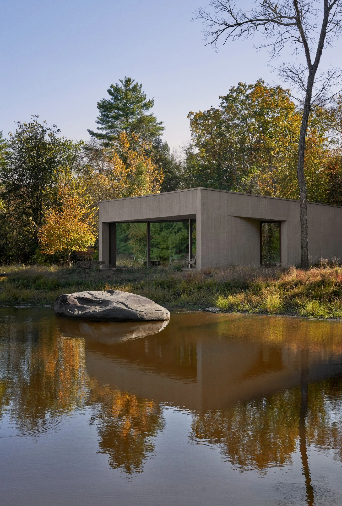Vipp Upstate by Johnston Marklee — A rendered concrete structure positioned at the water's edge of a pond reflects the surrounding autumn landscape.