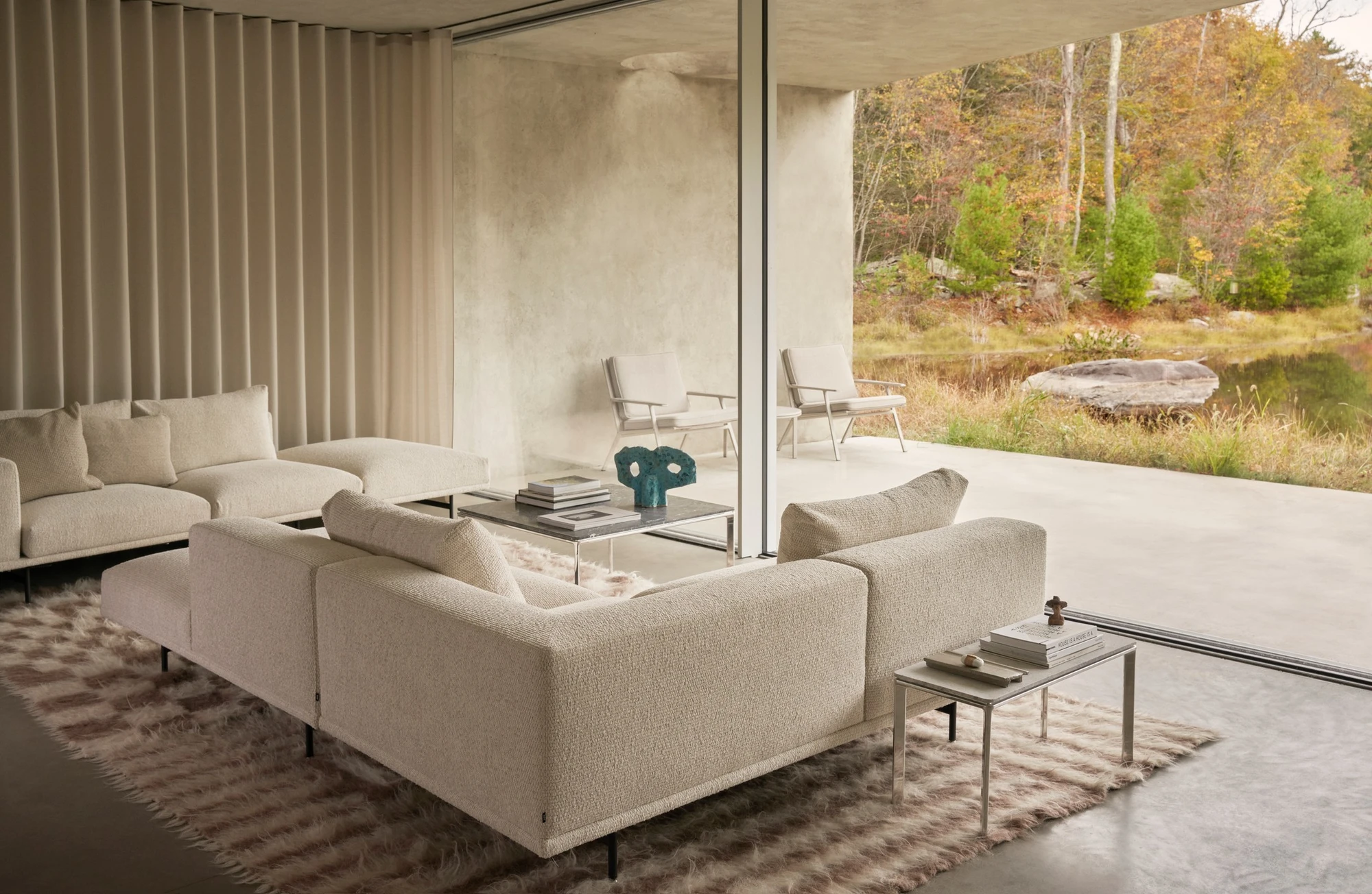Vipp Upstate by Johnston Marklee — The interior living space features a cream-colored upholstered sectional sofa positioned to frame views through floor-to-ceiling glass toward the...