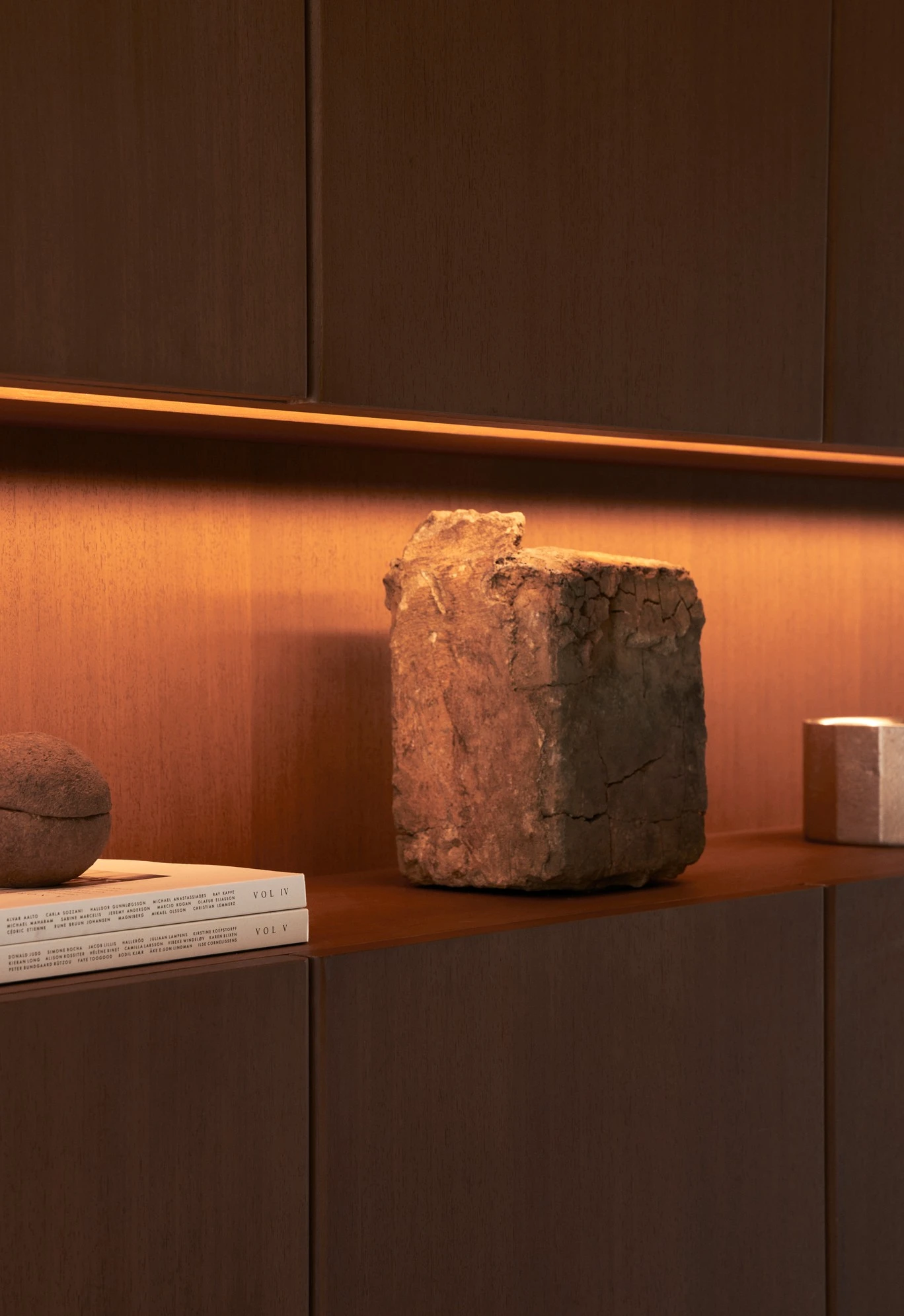 Vipp Upstate by Johnston Marklee — A rendered concrete shelf displays a weathered brick element and stacked volumes marked with roman numerals, their spines catching warm golden-hour light.