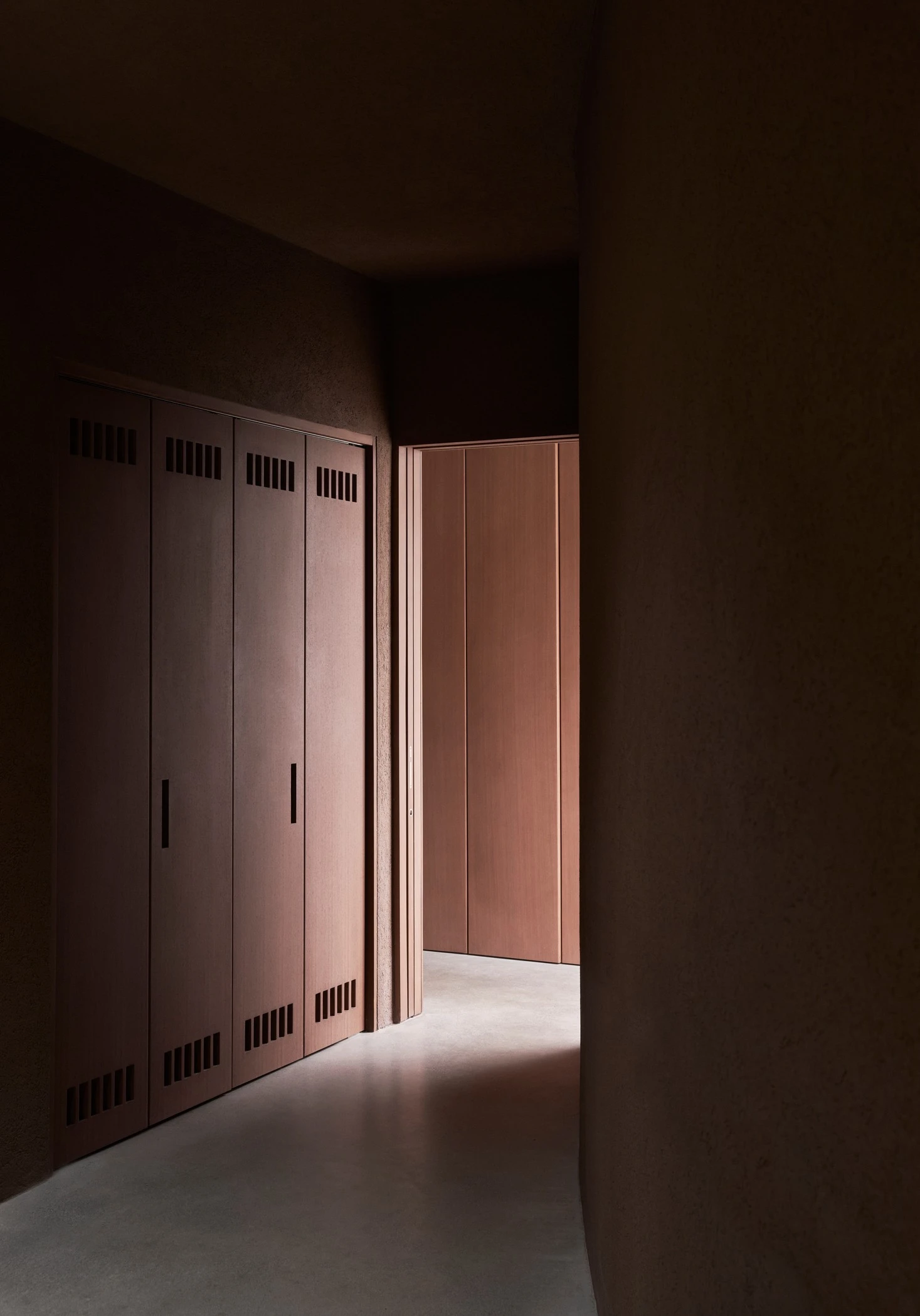 Vipp Upstate by Johnston Marklee — A rendered concrete corridor frames timber doors with dark hardware and ventilation grilles, their vertical grain echoing the wall's curved geometry.