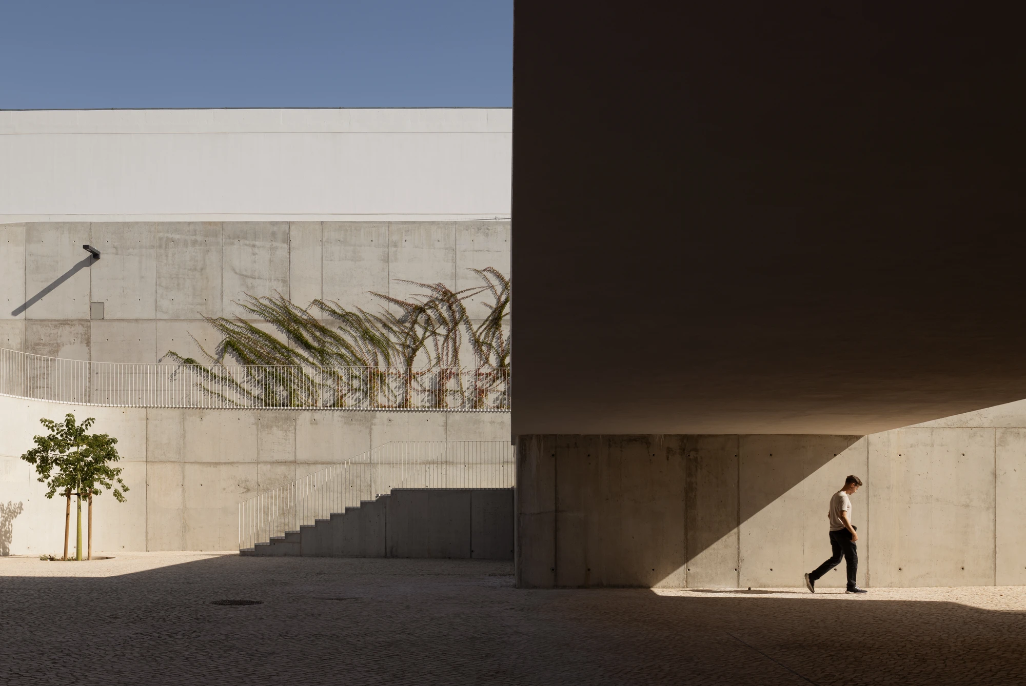 Da Boavista Church by Matos Gameiro arquitectos + atelier bugio — A jogger passes through the recessed staircase threshold of Da Boavista Church's monolithic concrete wall.