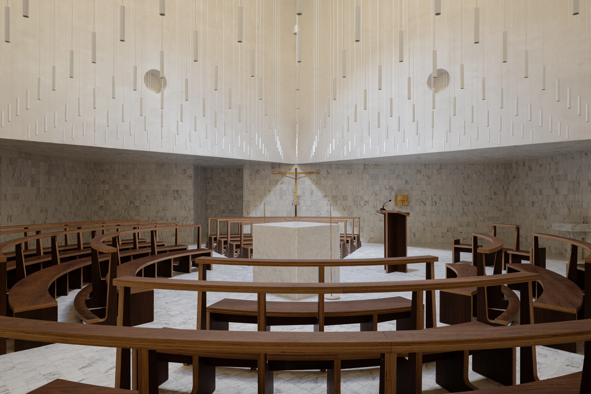 Da Boavista Church by Matos Gameiro arquitectos + atelier bugio — Interior view of Da Boavista Church reveals a circular seating arrangement of timber benches surrounding a central altar platform.