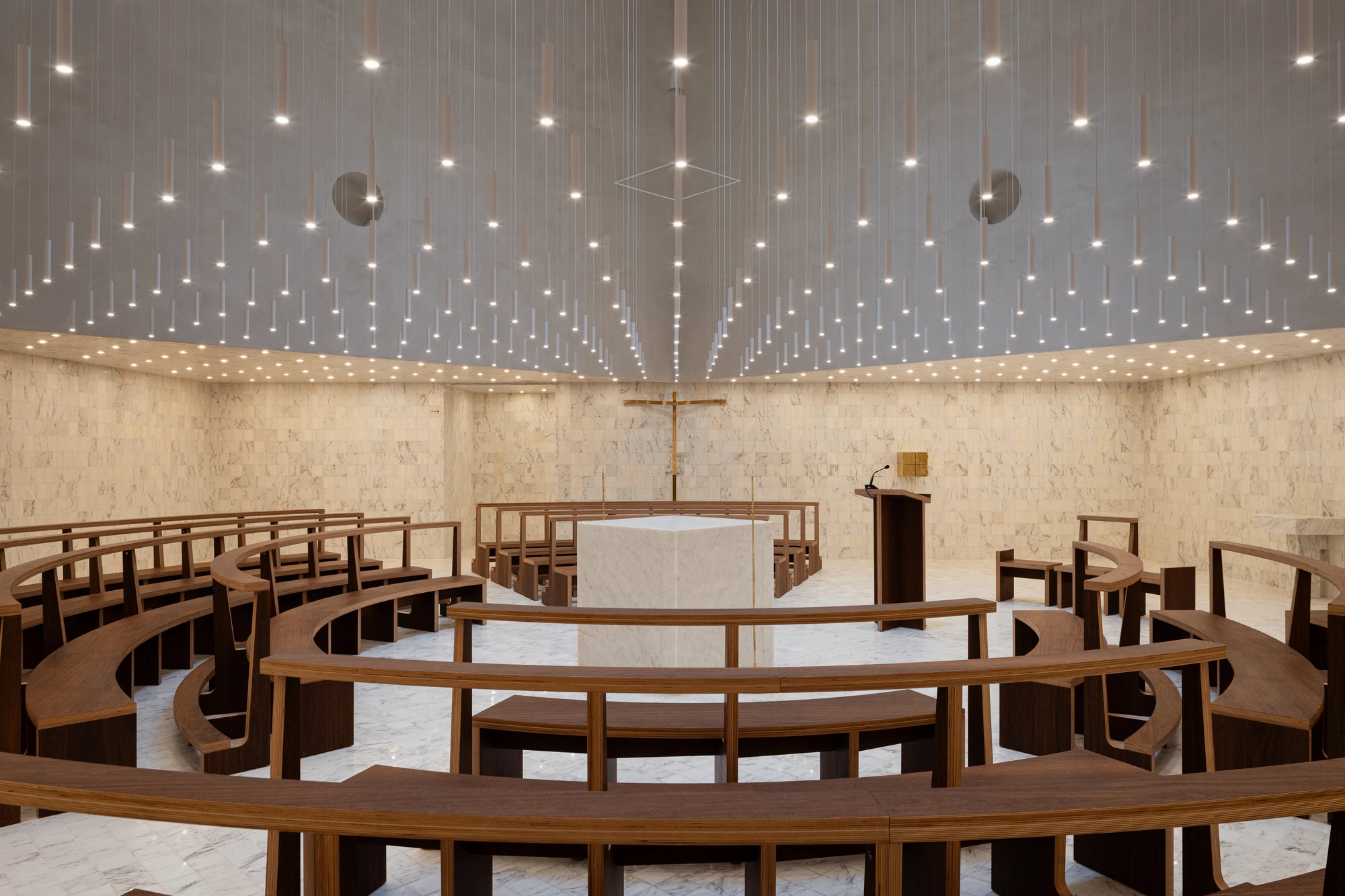 Da Boavista Church by Matos Gameiro arquitectos + atelier bugio — Interior of Da Boavista Church reveals a radial seating arrangement of curved timber benches facing a central altar platform.