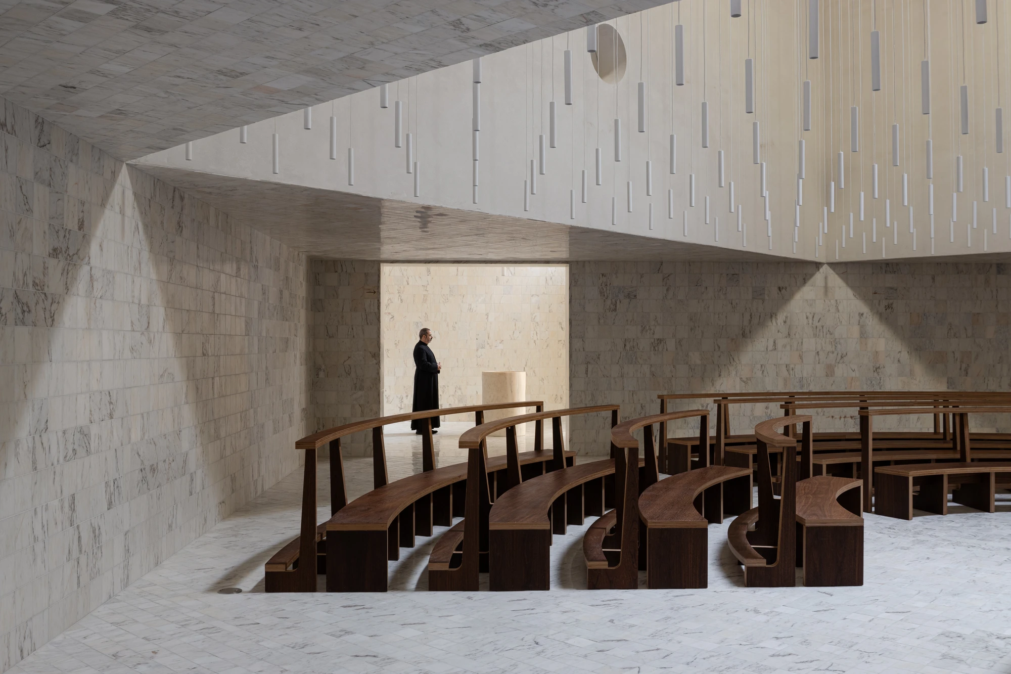 Da Boavista Church by Matos Gameiro arquitectos + atelier bugio — Interior view of Da Boavista Church's chapel space, where curved wooden pews with angled backrest supports establish a processional rhythm across the floor.