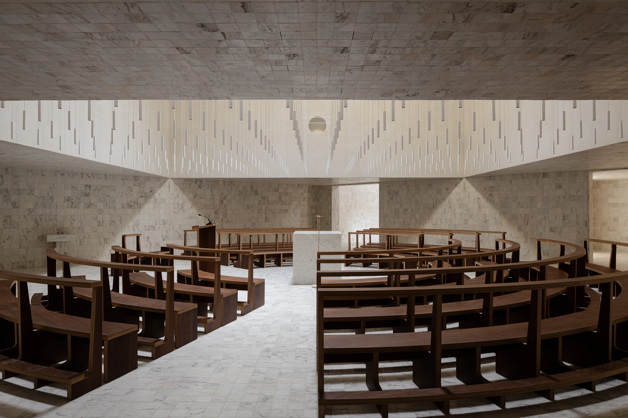 Da Boavista Church by Matos Gameiro arquitectos + atelier bugio — Interior of Da Boavista Church showing the nave arranged with curved wooden pews in concentric arcs facing a central altar.