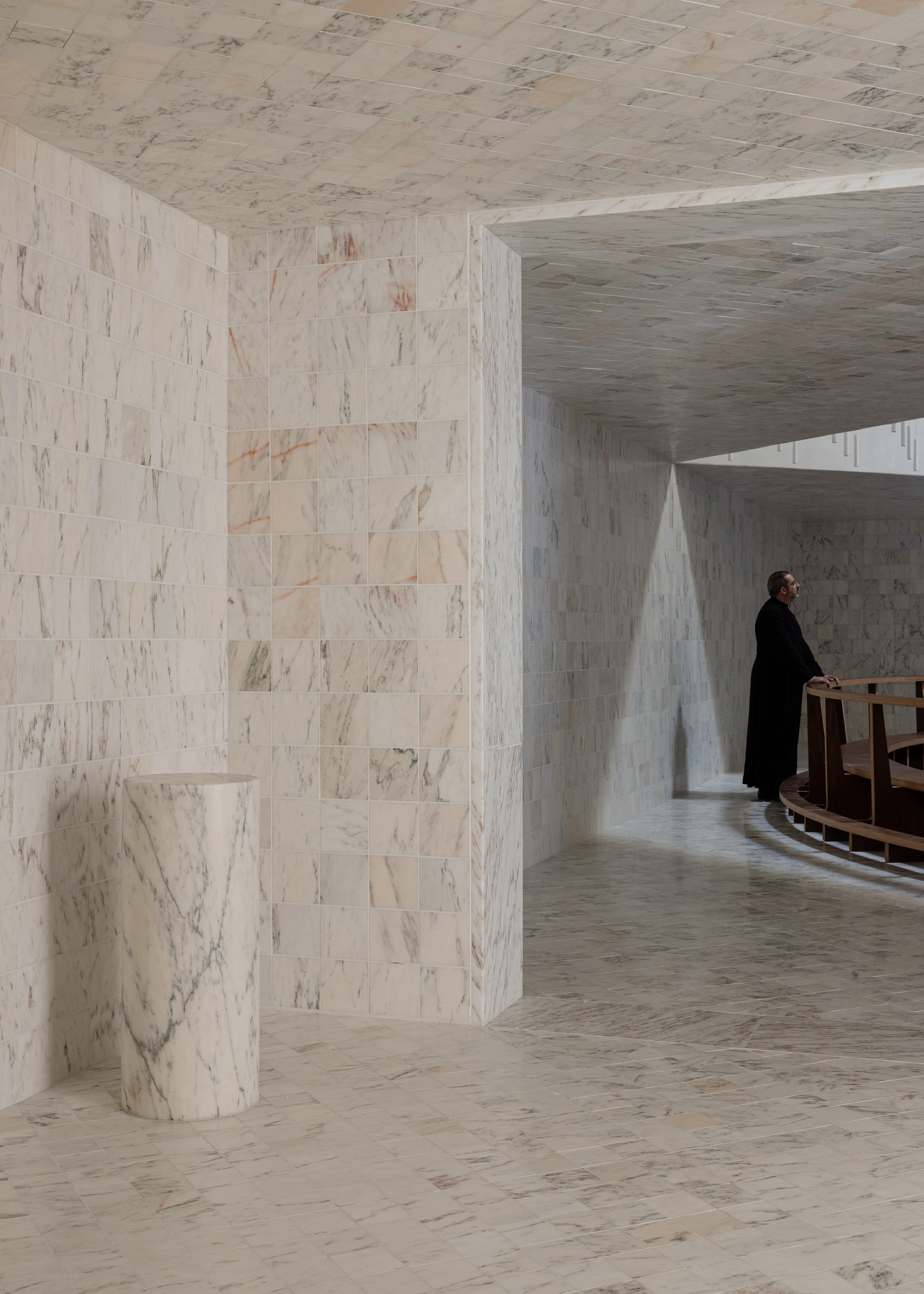Da Boavista Church by Matos Gameiro arquitectos + atelier bugio — Interior passage of Da Boavista Church reveals a monolithic marble-clad environment where cream-colored stone tiles with rust and grey veining cover walls,...