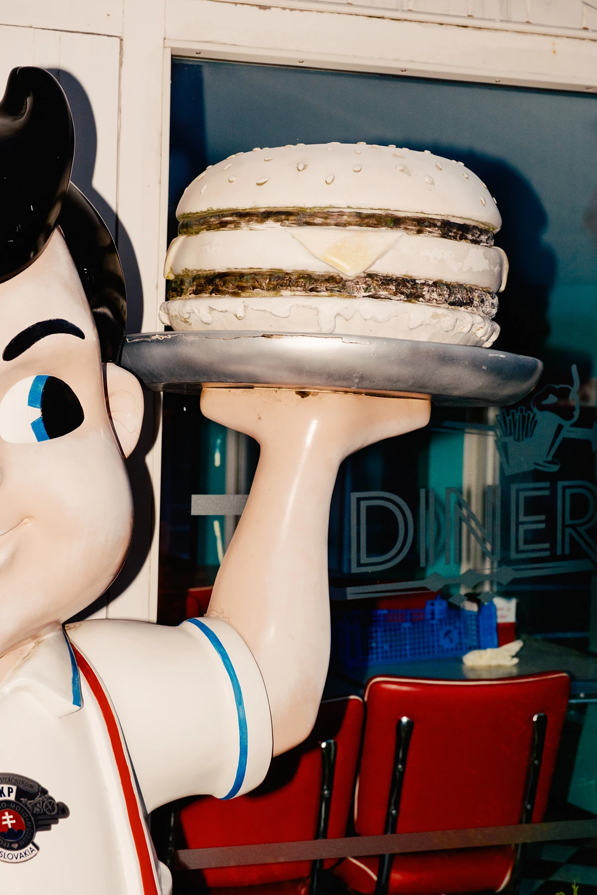 Lupine by Daniel Dorsa — A retro diner display featuring an oversized fiberglass server figure holding aloft a stacked hamburger sculpture.