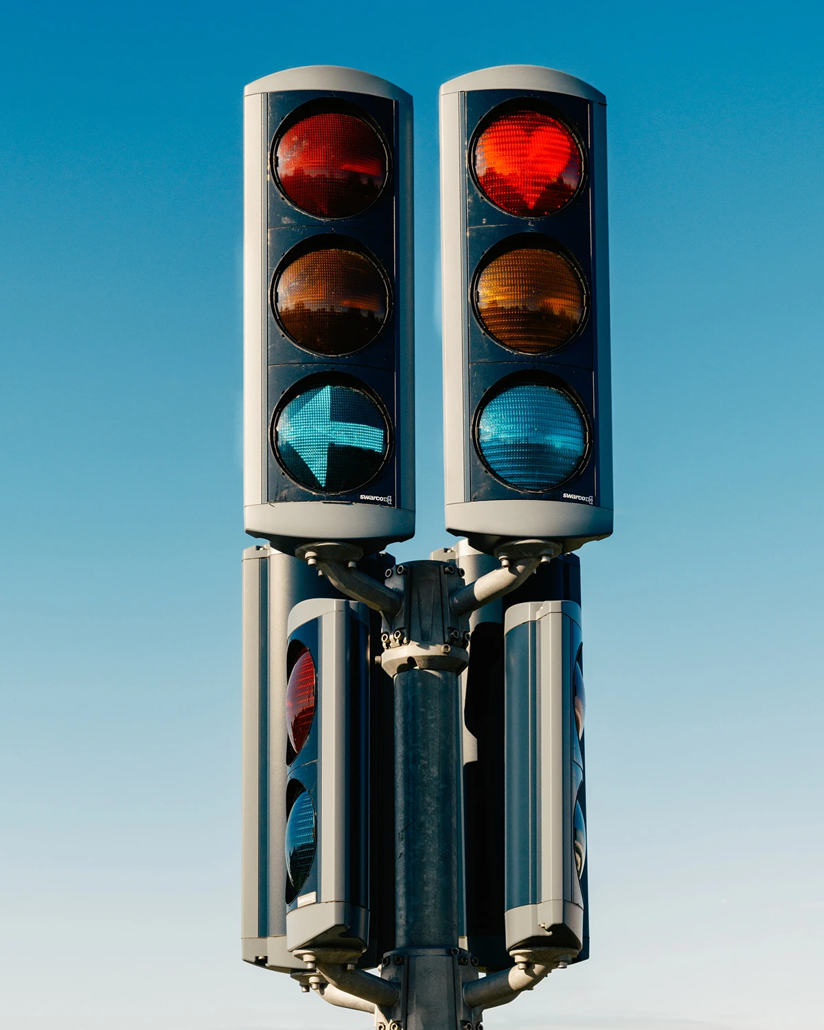 Lupine by Daniel Dorsa — Dual traffic signal units mounted on a cylindrical steel pole against clear blue sky.