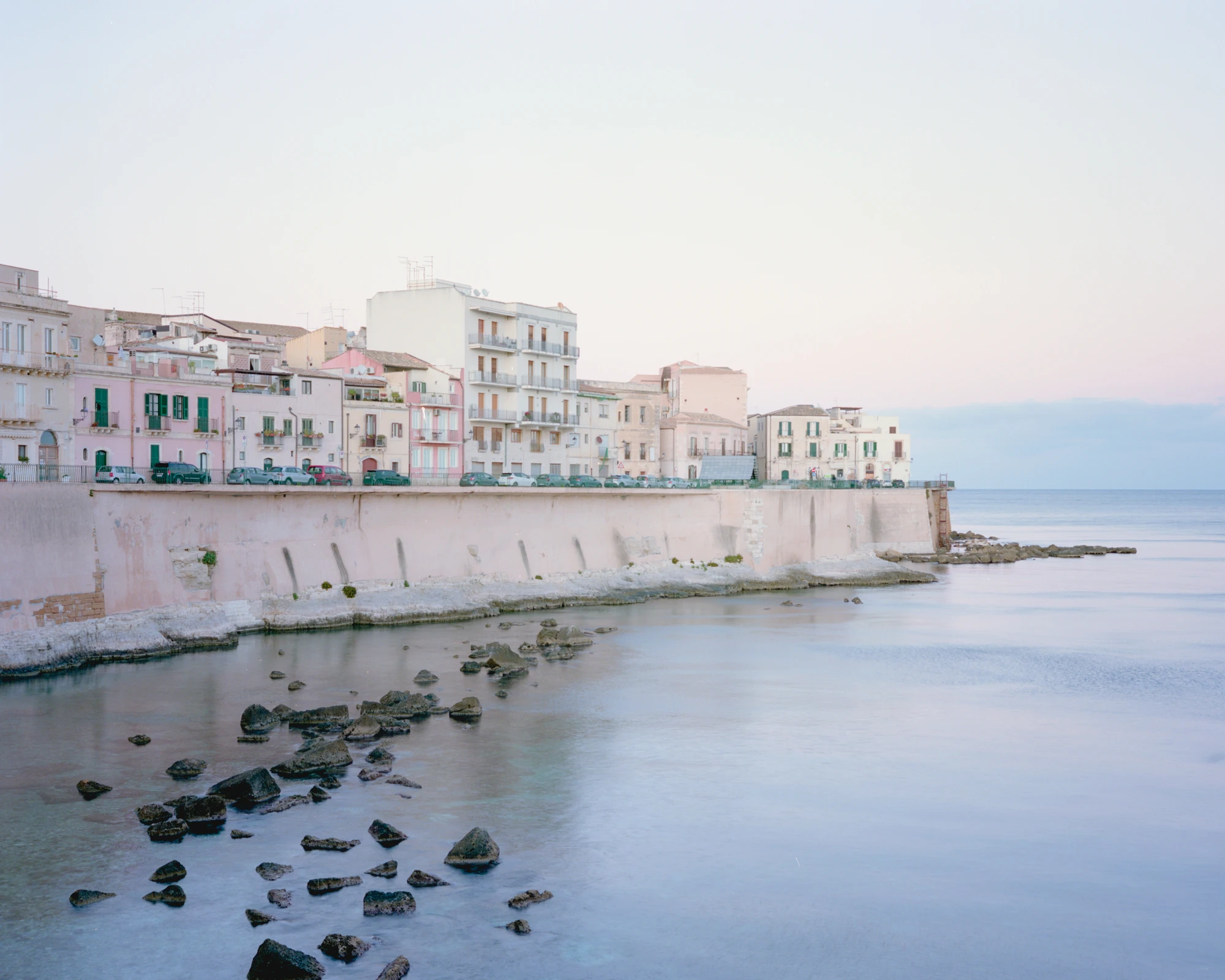 Pantalica Speculations by Leopold Banchini — This photograph documents the Ortigia waterfront, capturing the pastel-hued vernacular architecture of Sicily's historic settlement rising from a defensive...