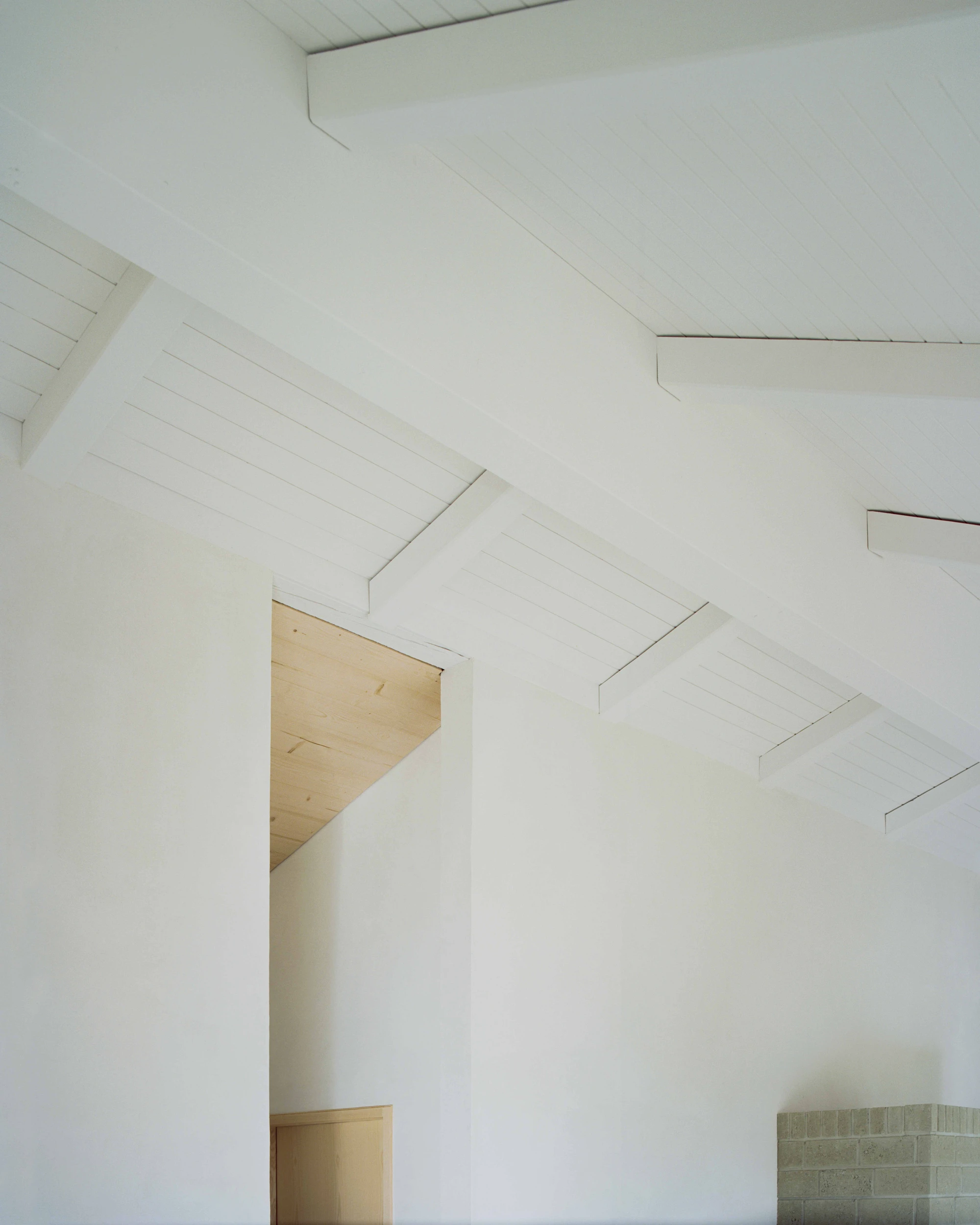 Family Villa by Noue Studio — A white plaster interior with exposed timber-framed roof structure and linear board detailing.