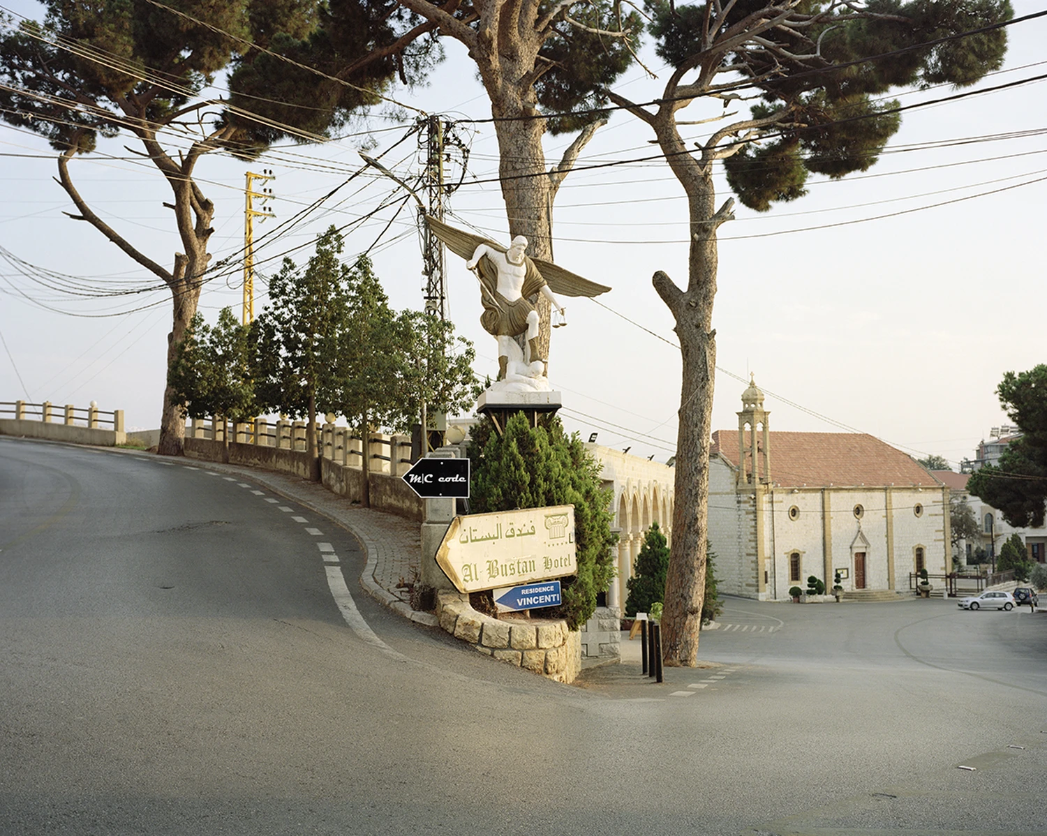 ASNAM (Idol Statues) by Georges Salameh — A white marble statue of the Virgin Mary dominates a street intersection in Lebanon, arms extended in benediction from a weathered stone pedestal.