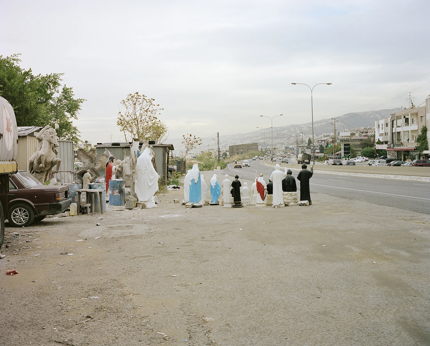 ASNAM (Idol Statues) by Georges Salameh — A processional gathering of white plaster and marble religious figures—including a crowned Virgin Mary with outstretched arms, robed saints, and smaller...
