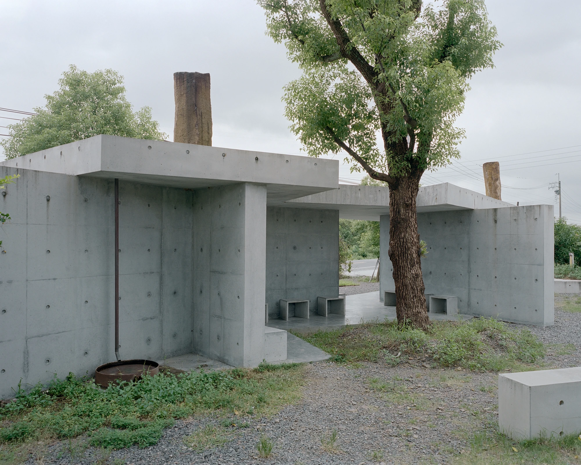 Entry Pavilion by metrics architecture studio — The entry pavilion demonstrates a modular concrete strategy, with L-shaped walls arranged to frame circulation and seating.
