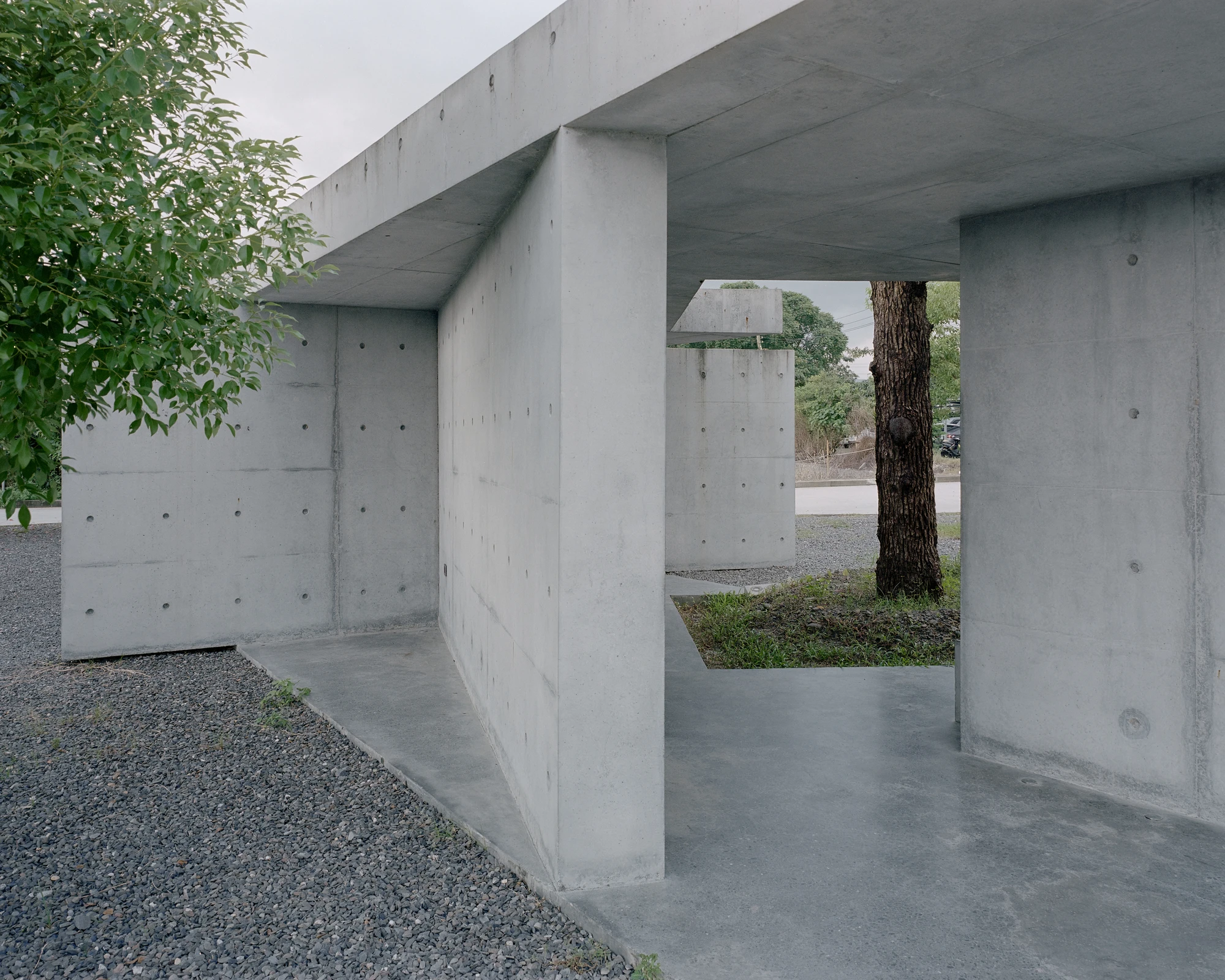 Entry Pavilion by metrics architecture studio — The entry pavilion's L-shaped concrete walls organize an open threshold, their monolithic forms punctuated by regular perforation patterns.