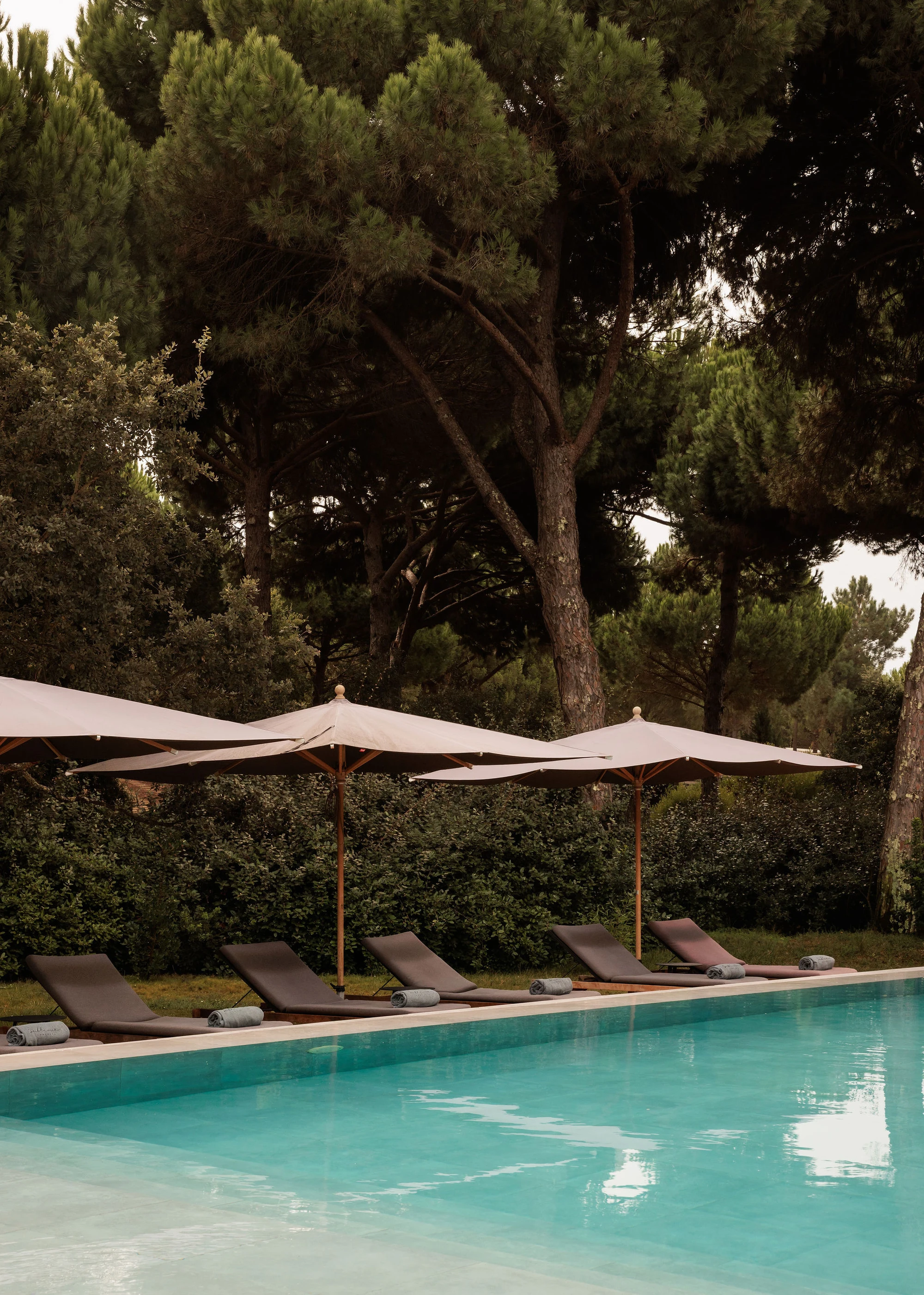 Sublime Comporta — A poolside leisure zone defined by geometric shadow patterns cast by mature pine canopy overhead.