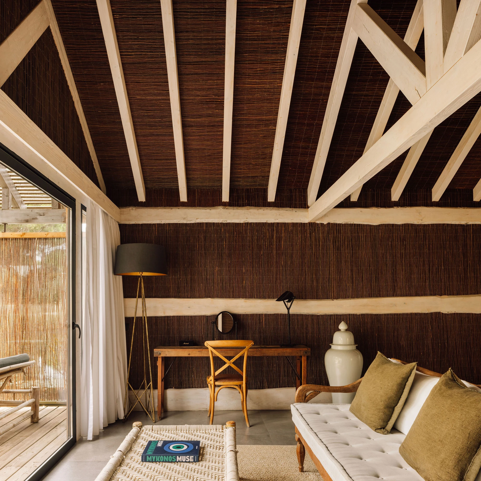 Sublime Comporta — Interior pavilion space featuring exposed timber beam structure with cream-painted cross-bracing against dark wood-clad ceiling.