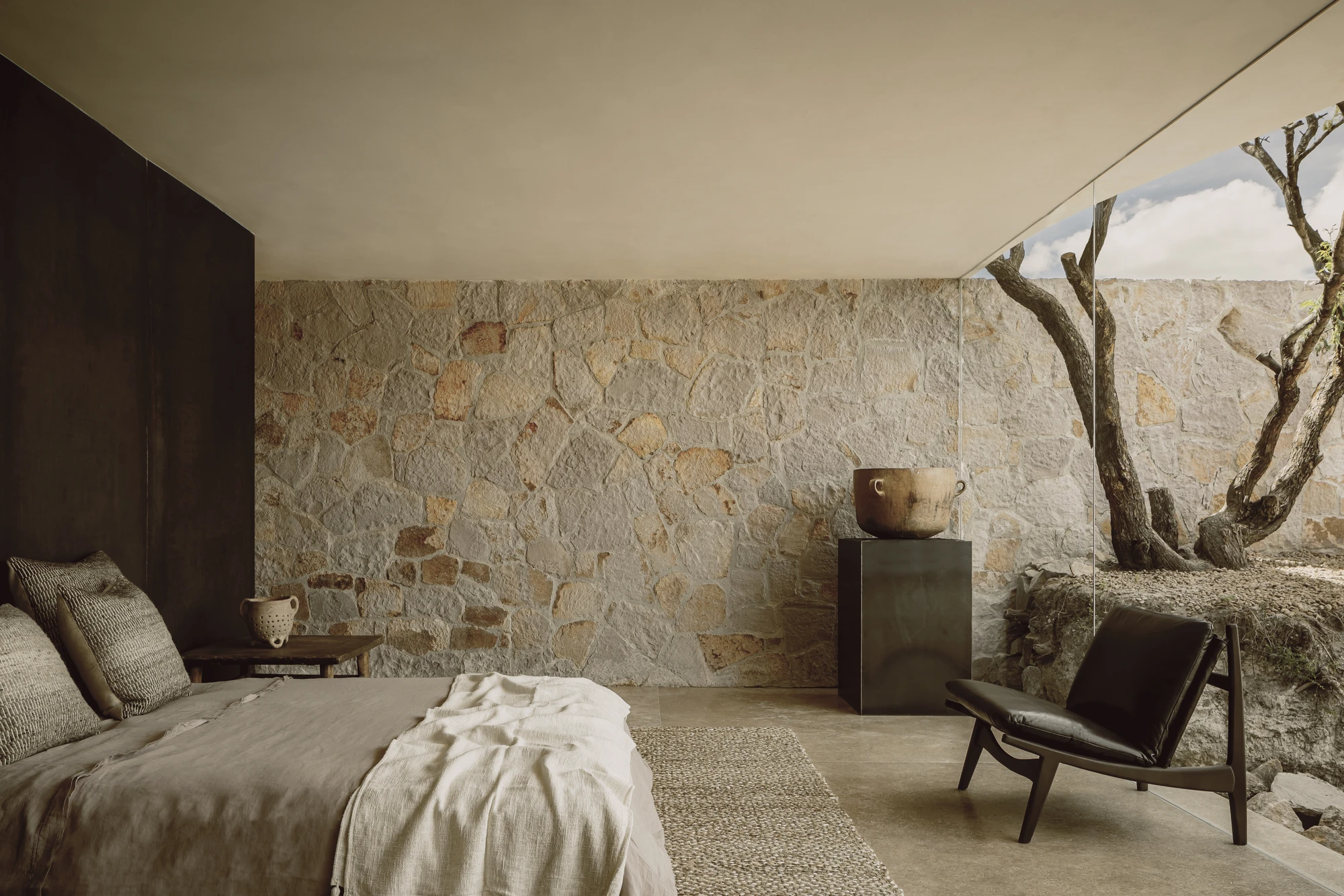 Enso House II by HW Studio — A bedroom interior carved from the site's existing stone mass, its thick coursed walls displaying horizontal geological stratification in cream and ochre tones.