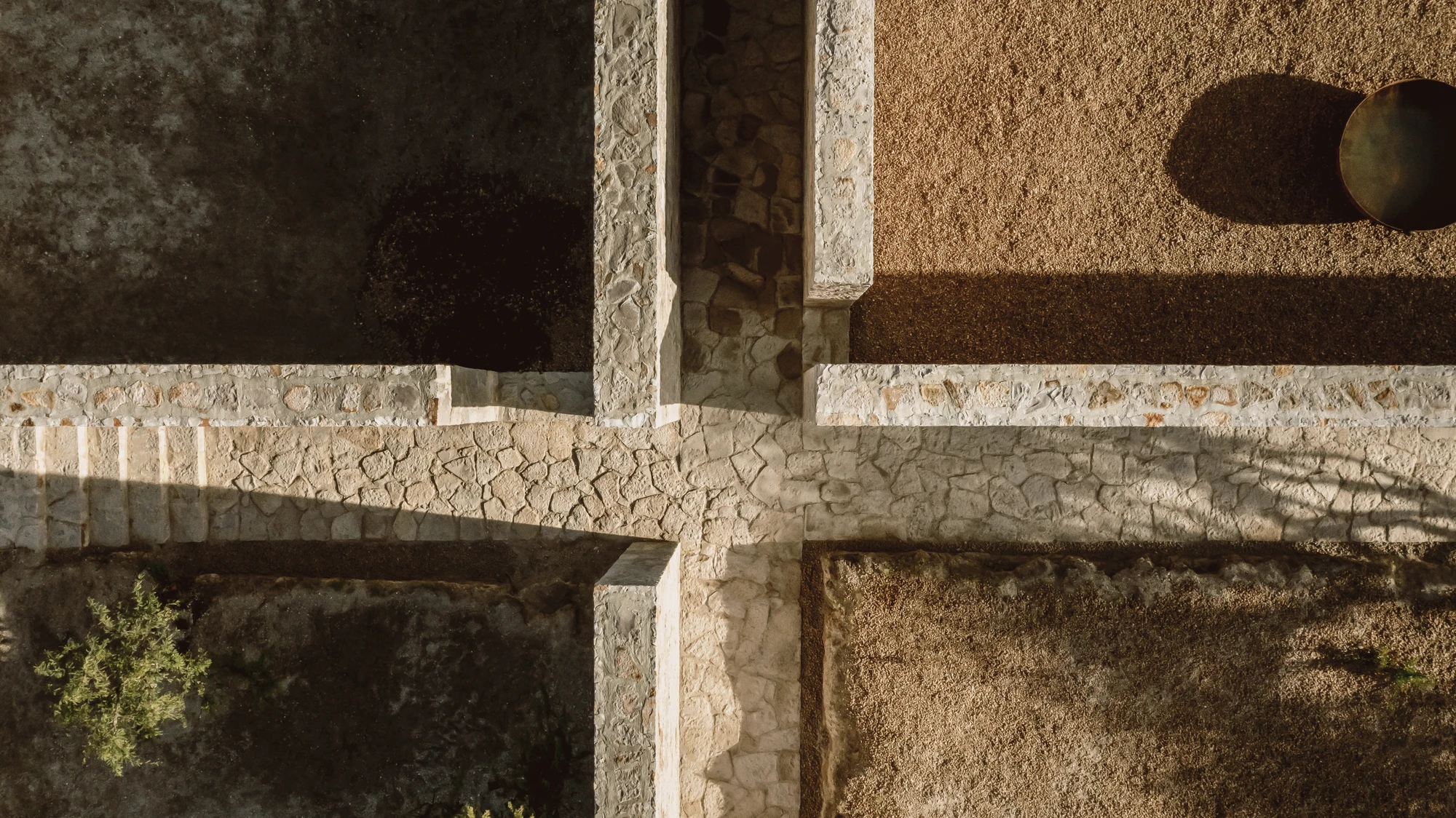 Enso House II by HW Studio — Overhead view of the cruciform plan's structural intersection, where coursed stone walls meet at right angles.