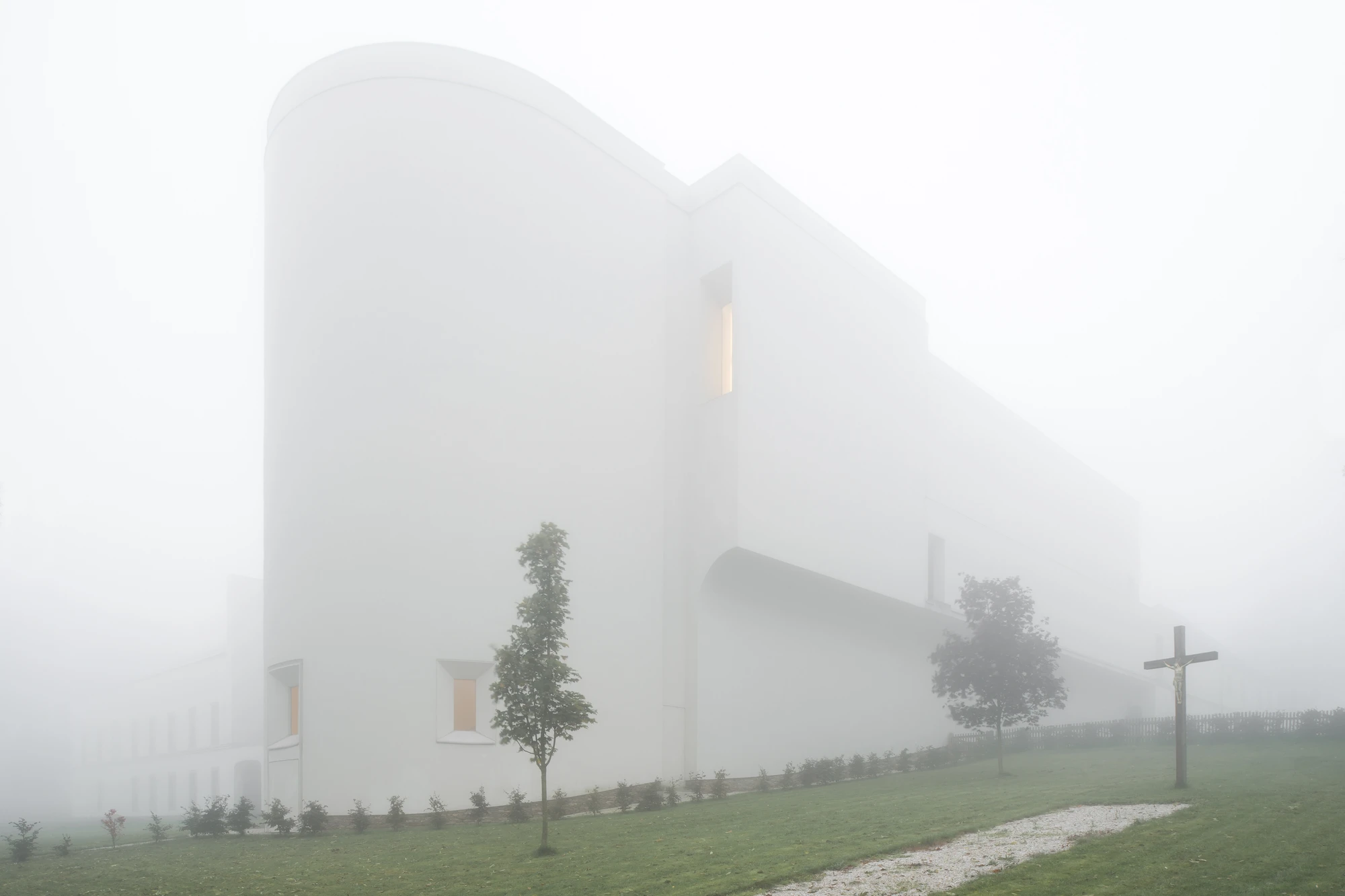 Abbey of Our Lady of Nový Dvůr by John Pawson — The monastery emerges from dense fog, its white rendered facade dissolving into the mist.