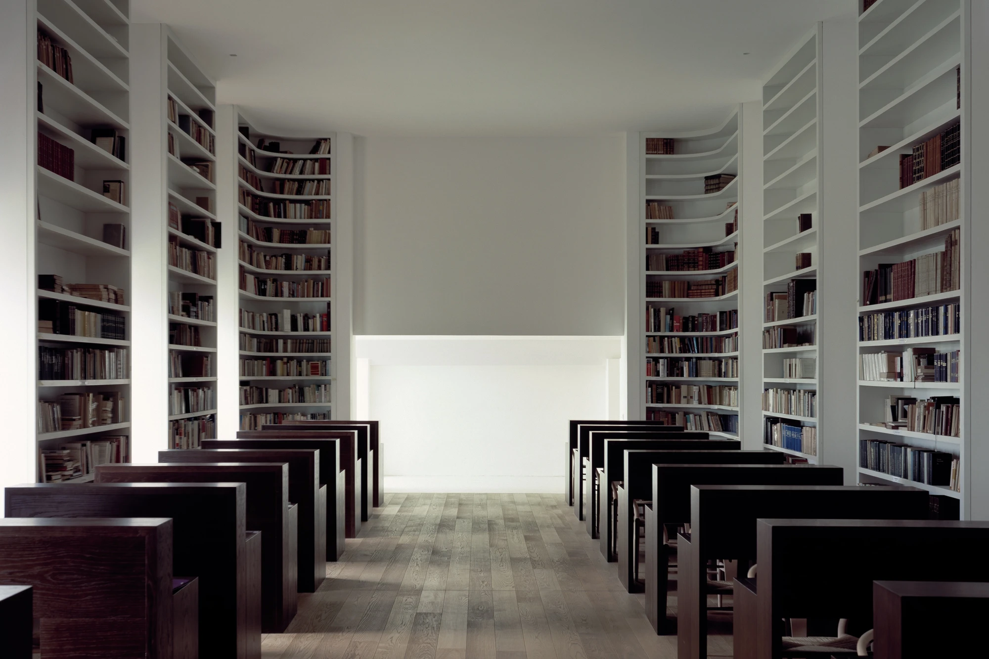 Abbey of Our Lady of Nový Dvůr by John Pawson — A library reading room lined with white timber shelving units arranged in rhythmic curved sections along opposing walls.
