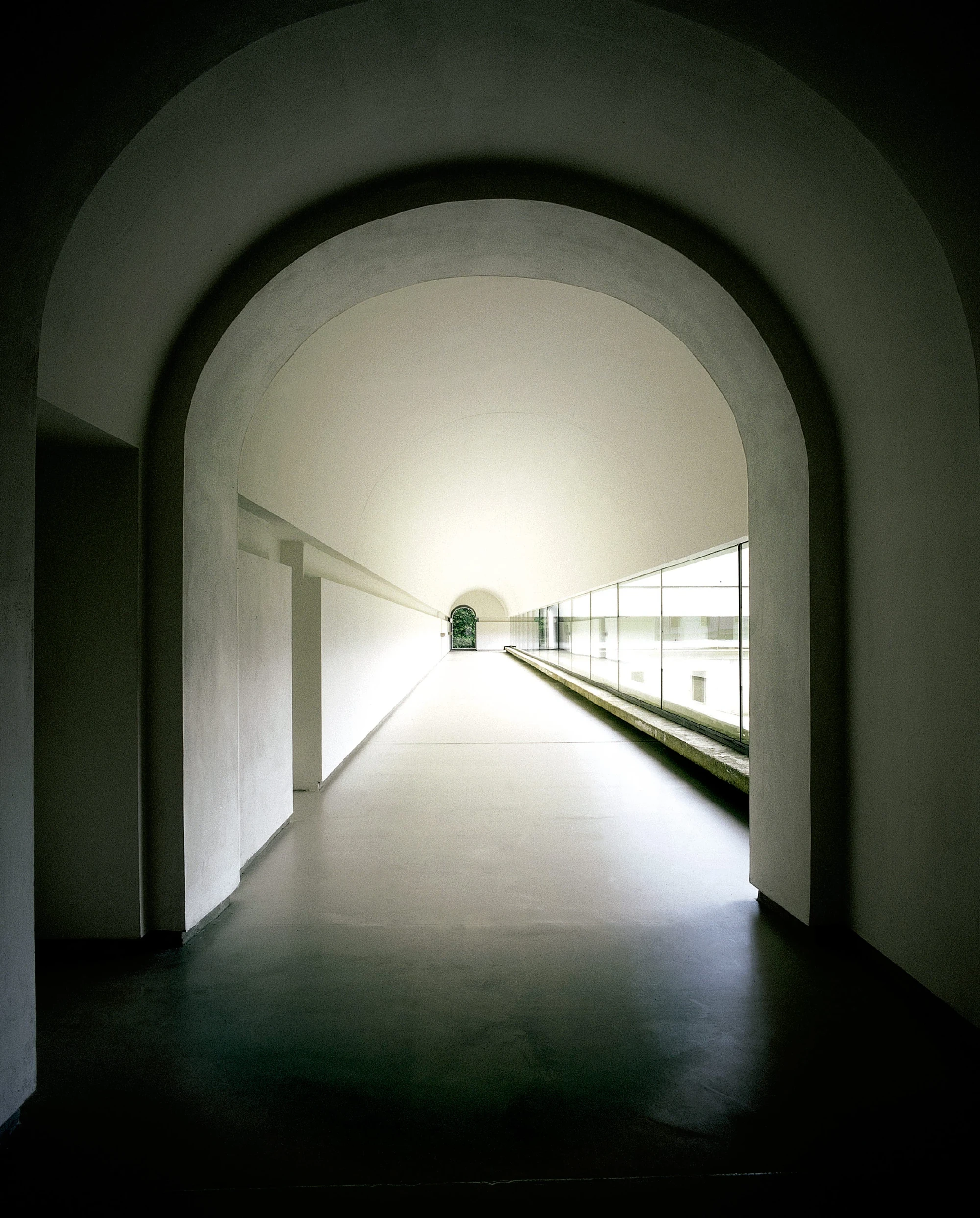 Abbey of Our Lady of Nový Dvůr by John Pawson — A barrel-vaulted corridor extends toward diffuse natural light, its continuous arched ceiling rendered in white plaster.