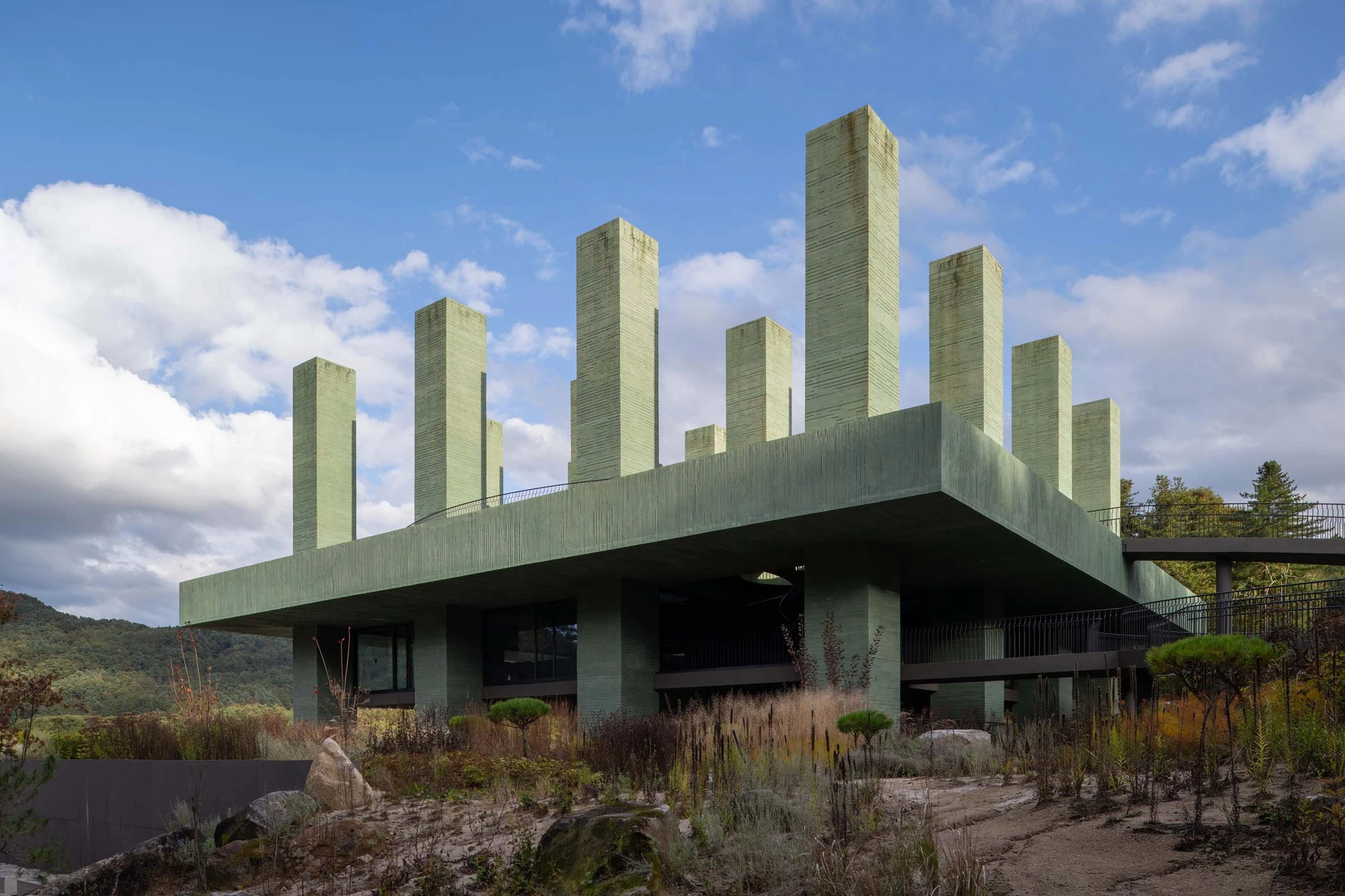 REST Garden Restaurant by Pezo von Ellrichshausen — Nine rectangular concrete columns arranged in a strict orthogonal grid rise from a cantilevered platform elevated above sloped terrain.