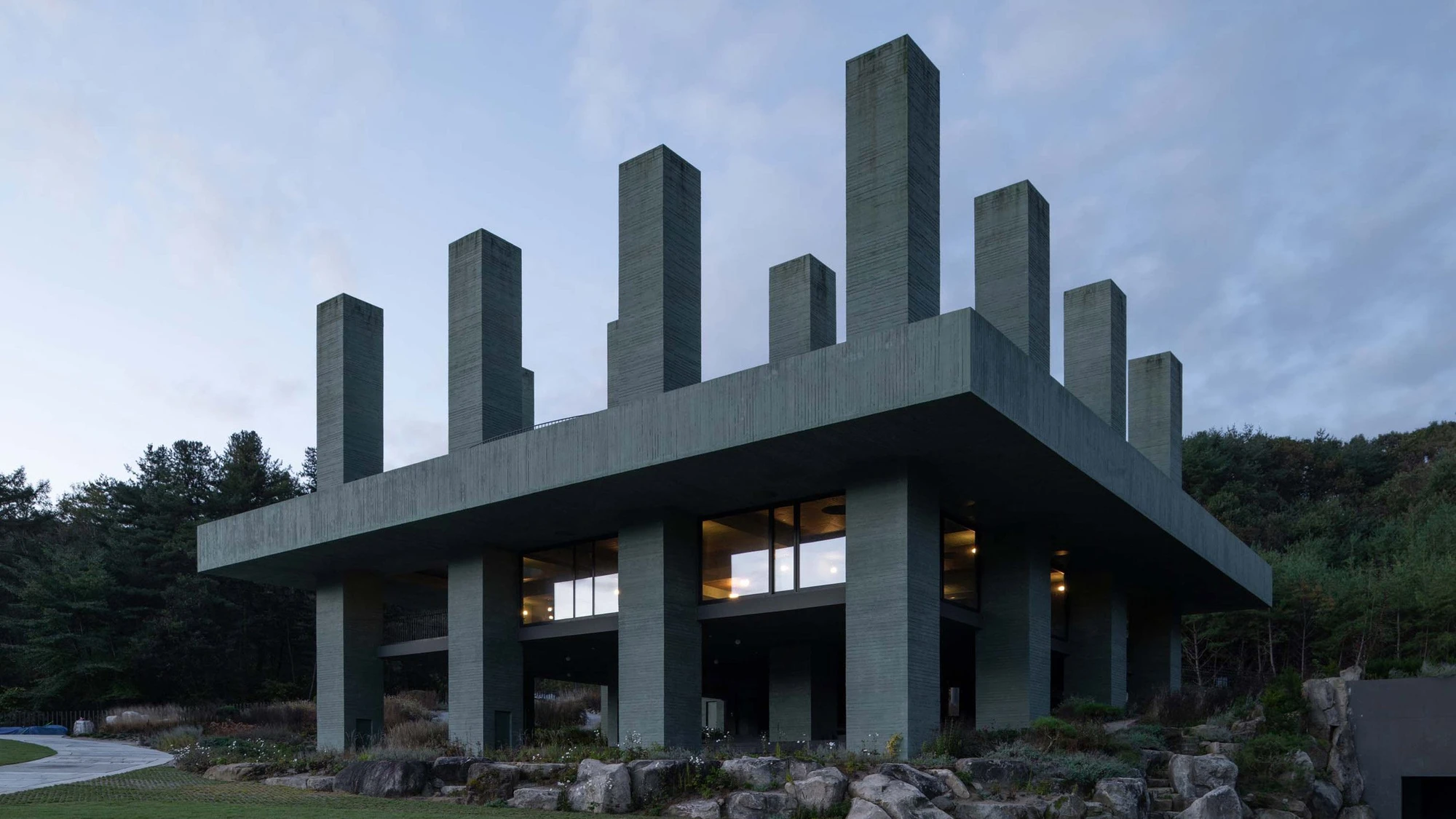 REST Garden Restaurant by Pezo von Ellrichshausen — Nine rectangular concrete columns rise in strict grid formation from a cantilevered platform, their soft green-tinted surfaces marked by dark vertical striping.