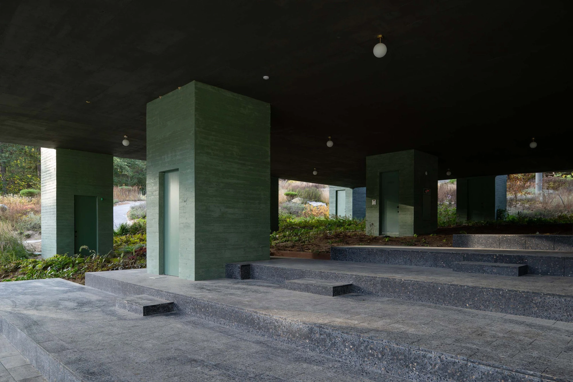 REST Garden Restaurant by Pezo von Ellrichshausen — Nine monolithic concrete columns arranged in a rigid grid stand beneath a continuous black ceiling plane, their surfaces finished in soft green-tinted...