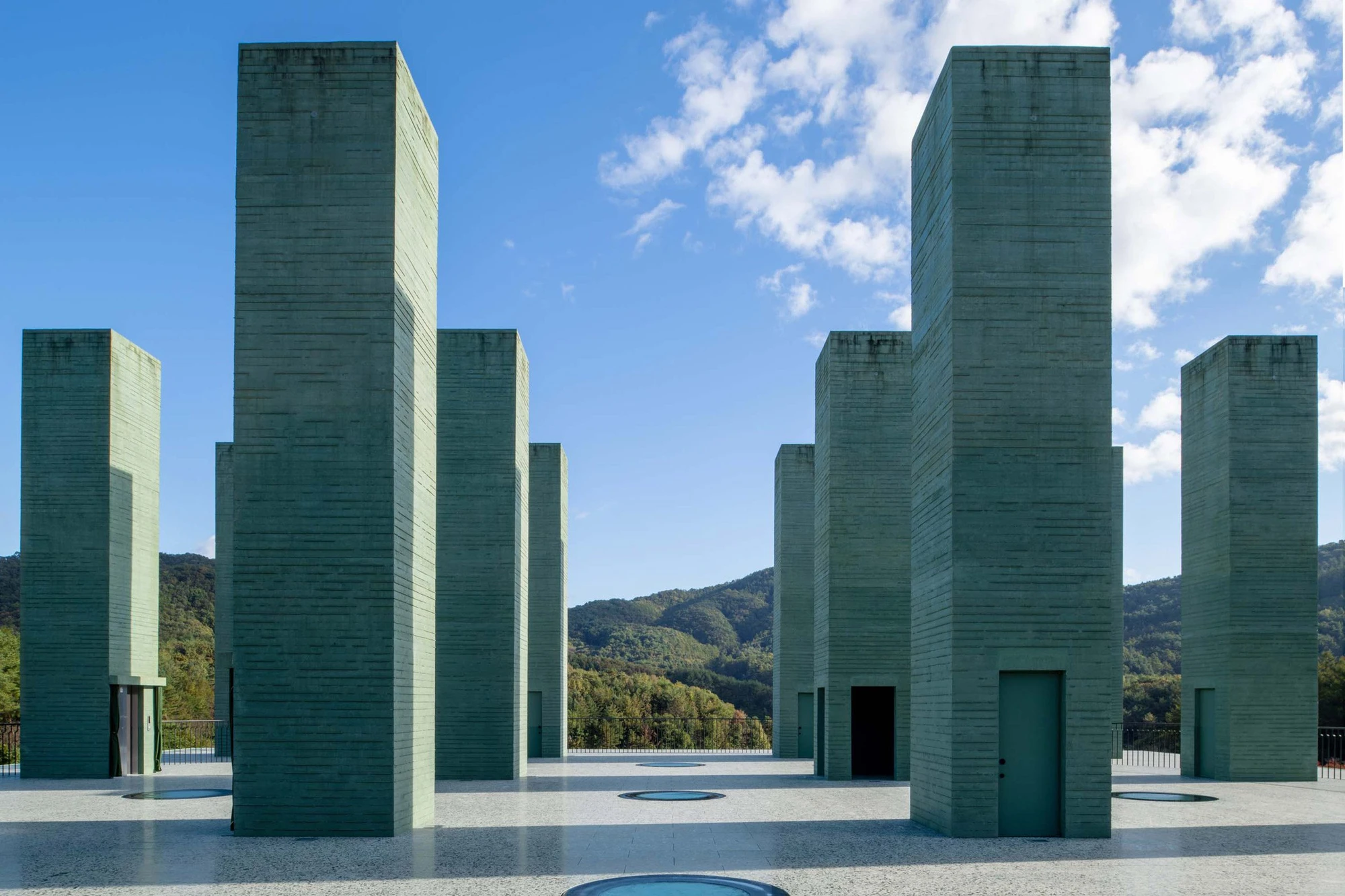 REST Garden Restaurant by Pezo von Ellrichshausen — Nine rectangular concrete columns arranged in a strict grid dominate the elevated platform, their soft green-tinted surfaces marked by dark vertical...
