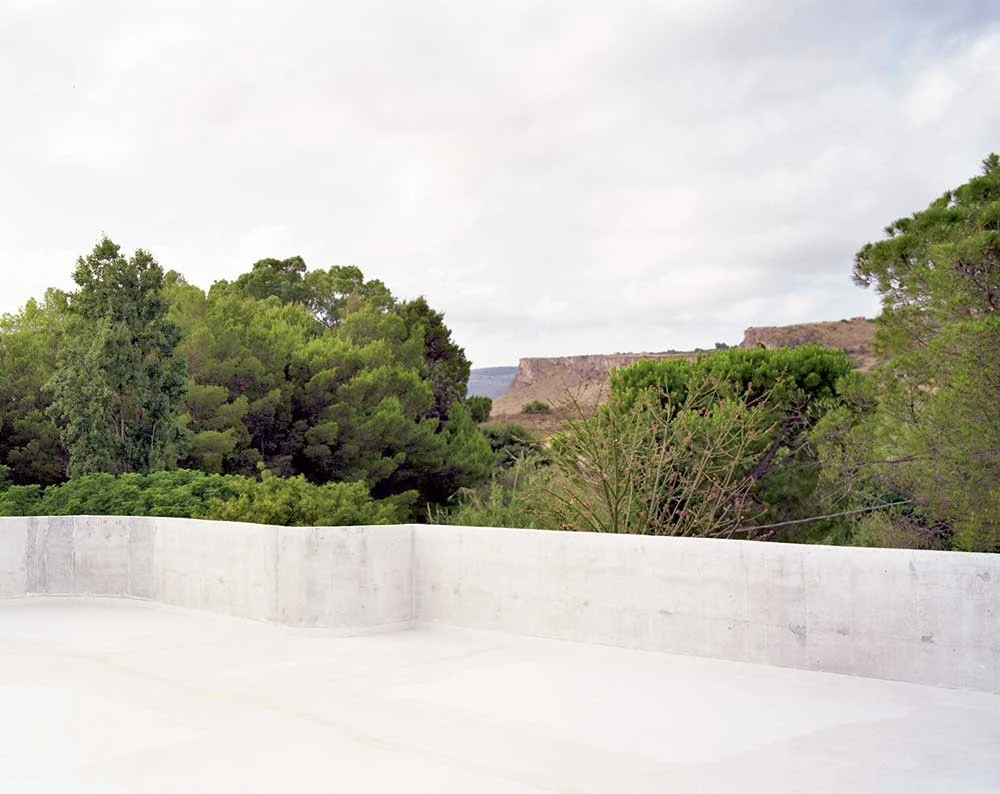 Guardia di Finanza by Brandlhuber+ — A concrete courtyard frames the hillside landscape beyond.