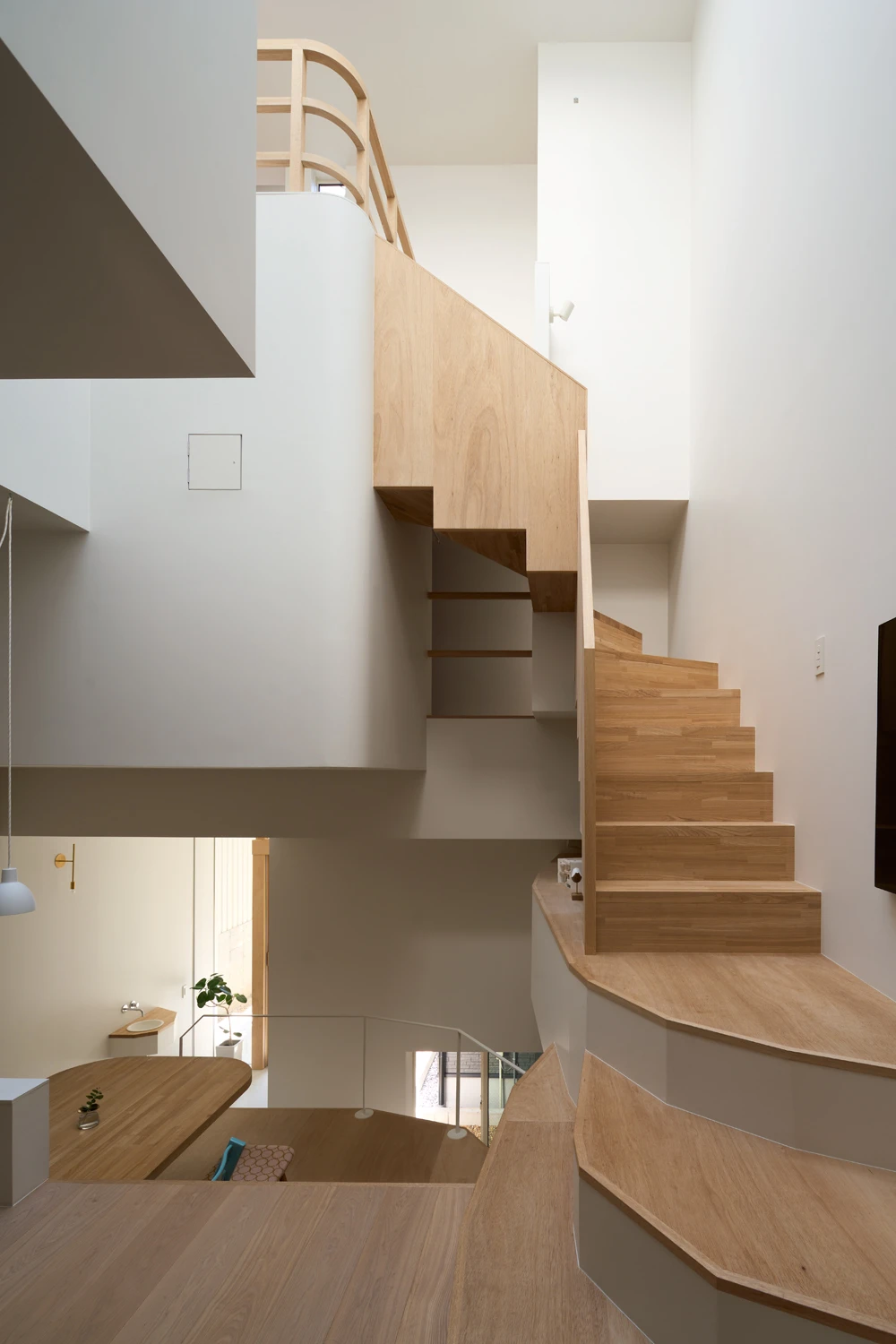 House in Hirano by Fujiwaramuro Architects — Interior view of a multi-story timber staircase ascending through a narrow vertical void.