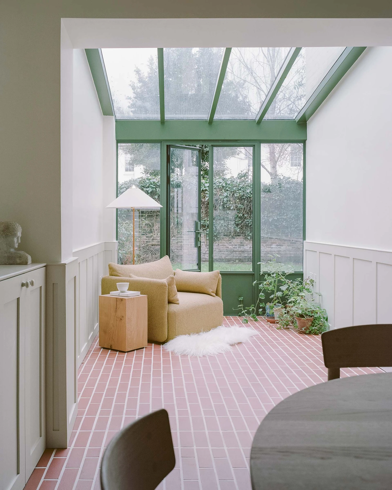 Barnsbury House by Architecture for London — A sunlit conservatory extension frames a ochre-upholstered armchair positioned beneath a grid of skylight panels.