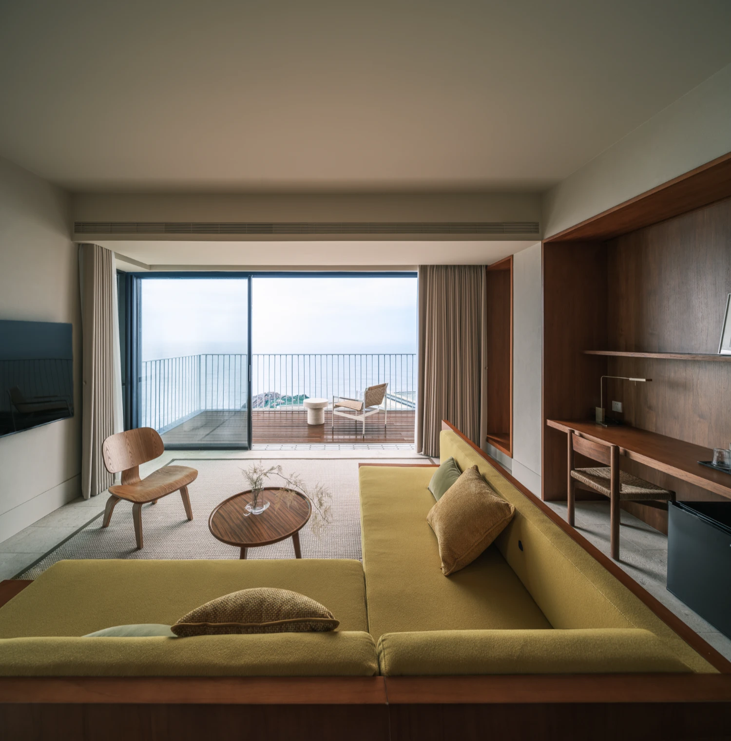 Lost Villa Shengsi Huanglong Island Lighthouse Hotel by SZ-Architects — A hotel suite frames the seascape through floor-to-ceiling glazing, its interior organized around a mustard-yellow sectional sofa positioned in the foreground.