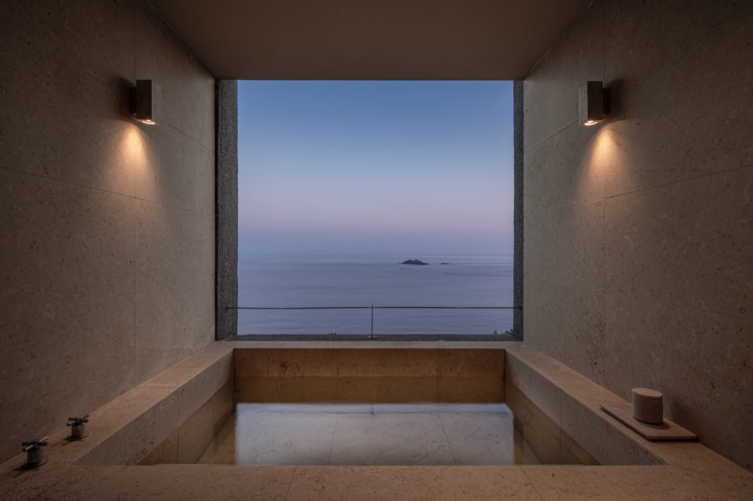 Lost Villa Shengsi Huanglong Island Lighthouse Hotel by SZ-Architects — A sunken bathtub carved into travertine occupies the foreground of this double-height interior, its recessed basin framed by stone ledges.