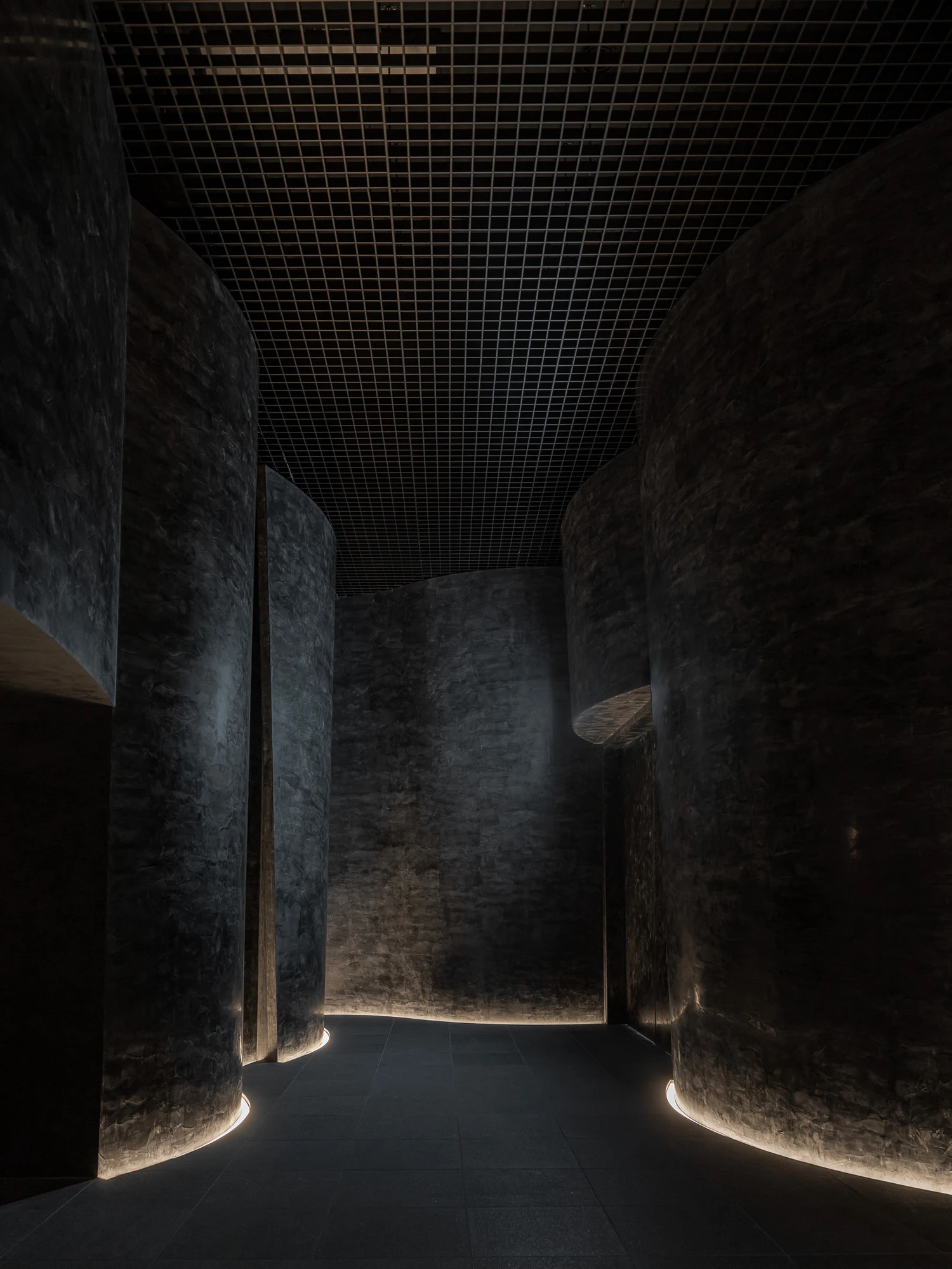 Baekje Gilt Bronze Incense Burner Hall (Buyeo National Museum) by WGNB — A passage defined by two monolithic curved concrete walls, their aggregate surfaces weathered and textured, converges toward a bright threshold.