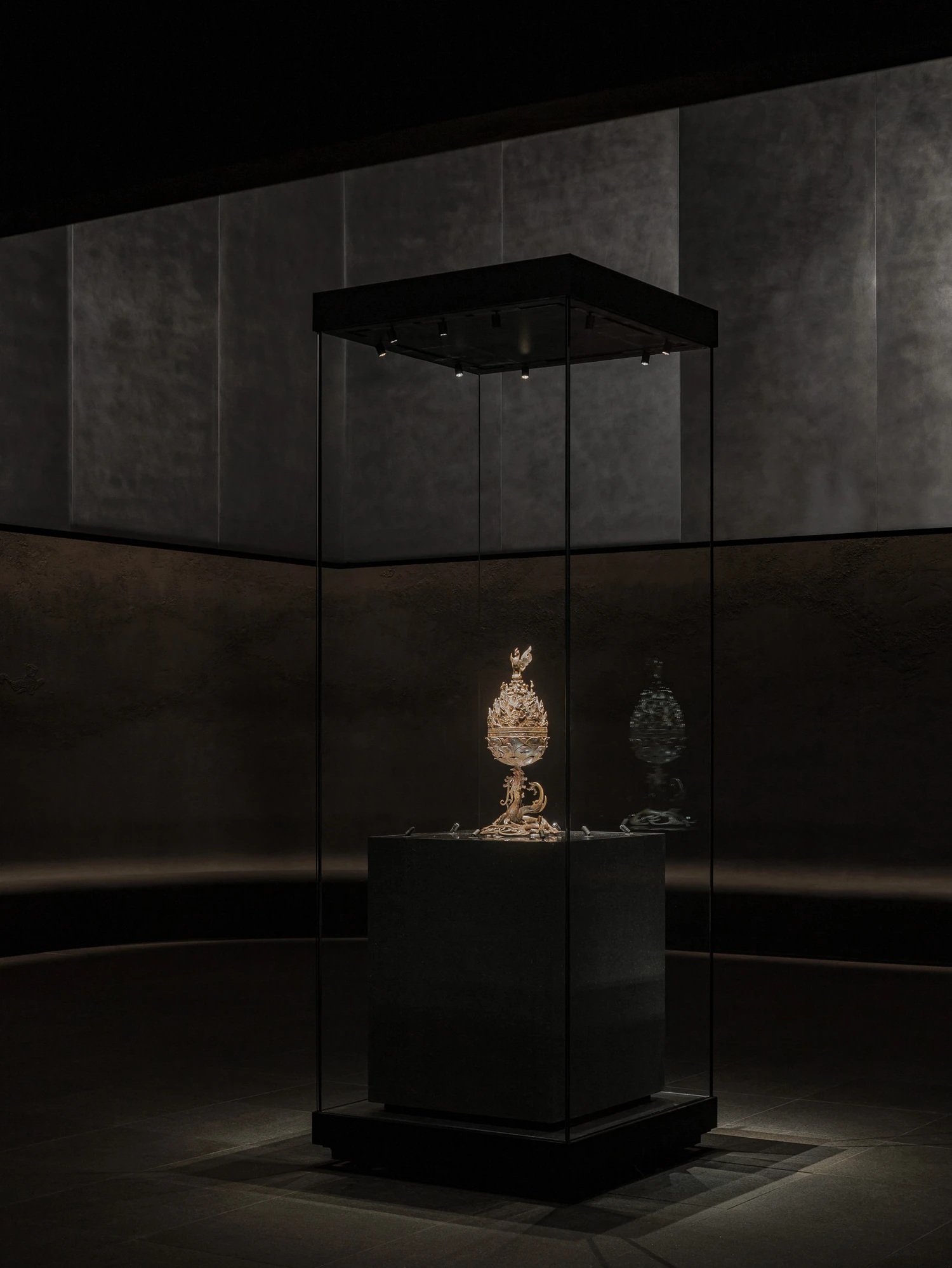 Baekje Gilt Bronze Incense Burner Hall (Buyeo National Museum) by WGNB — A glass vitrine occupies the center of a curved concrete hall, its black metal frame and ceiling contrasting against weathered aggregate walls.